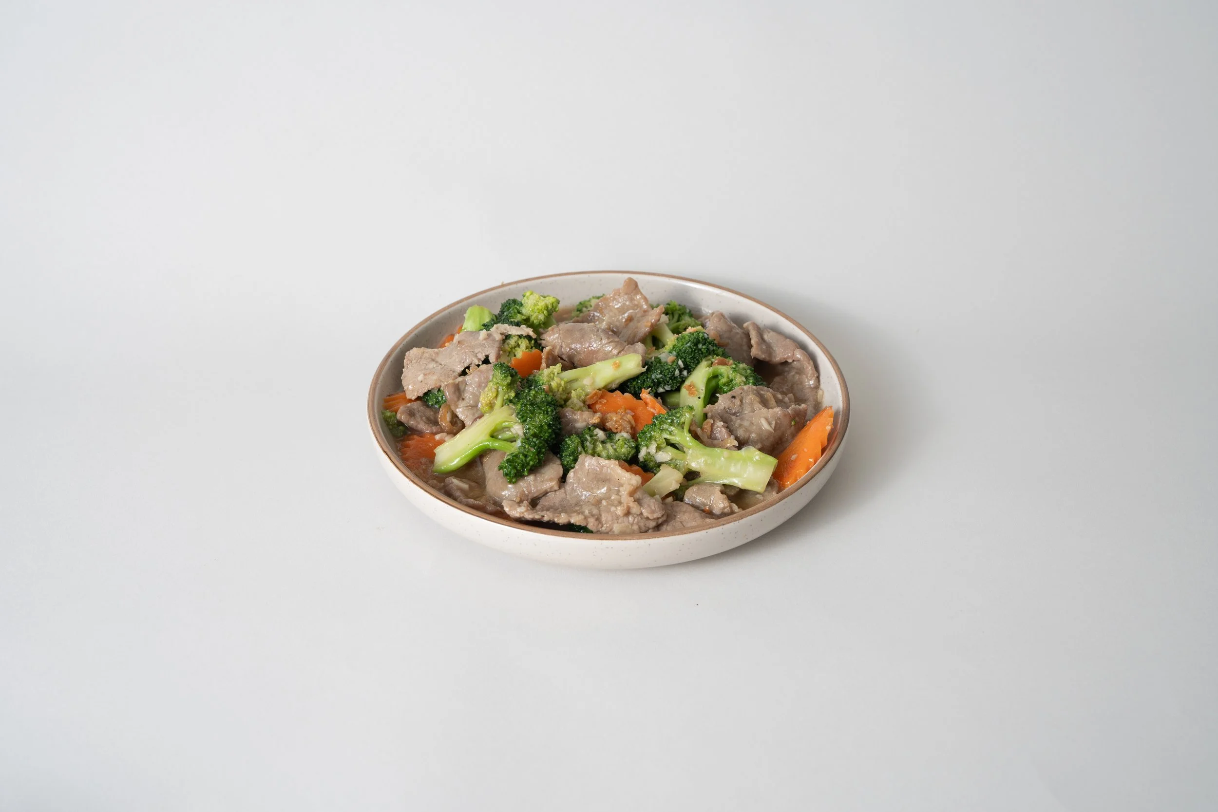 A bowl of beef and broccoli stir-fry with carrots on a plain white background.