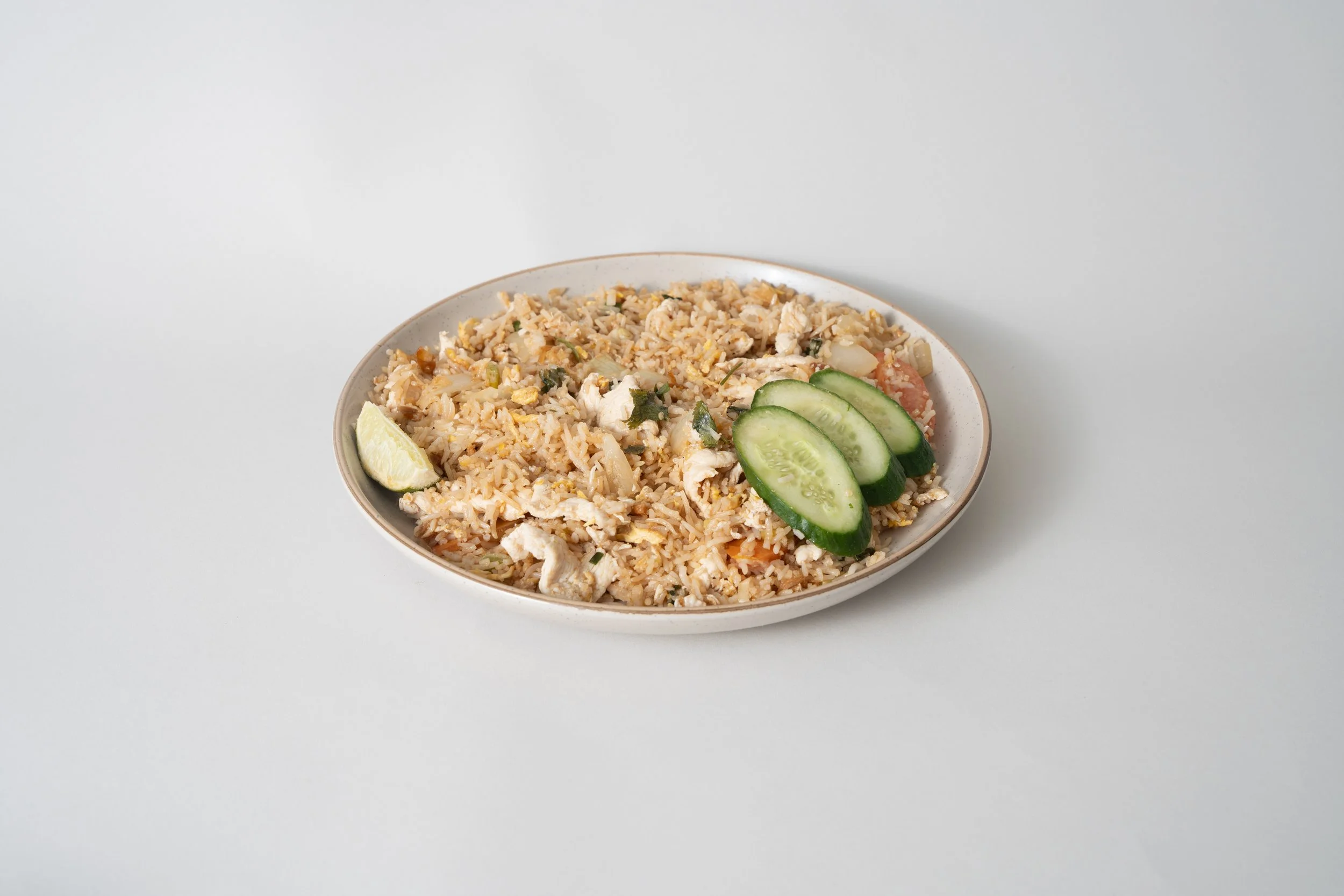 Plate of fried rice garnished with cucumber slices and a lime wedge on a plain white background.