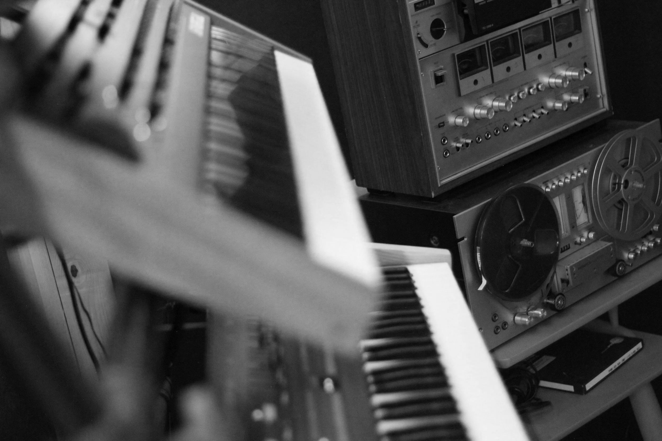 Black and white photo of vintage audio equipment including a keyboard, reel-to-reel tape recorder, and various audio control devices.