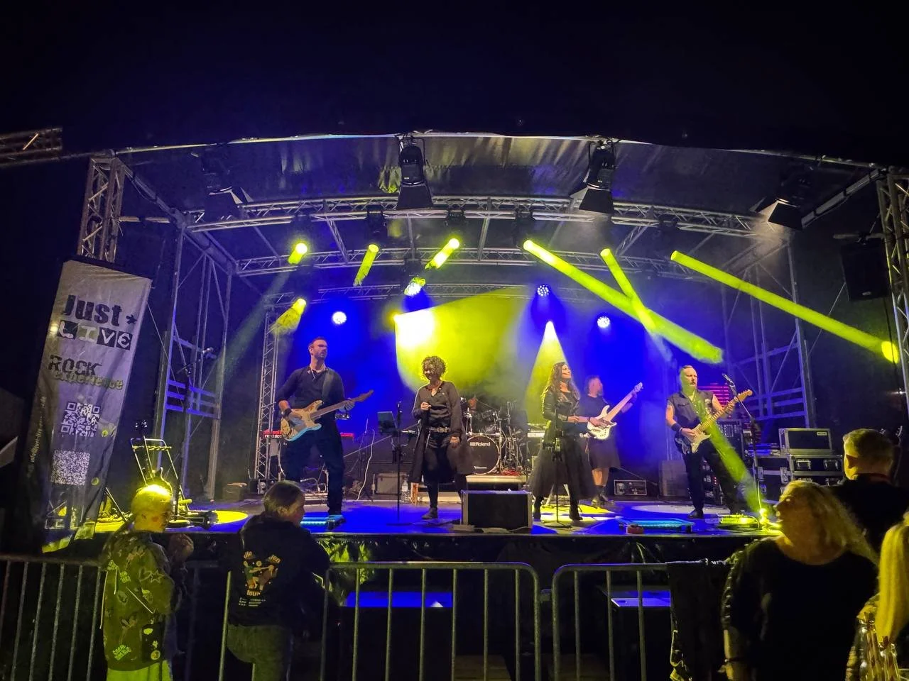 Band auf einer Bühne mit Gelb- und Blaulicht, live Musik, Abendkonzert, Publikum im Vordergrund.