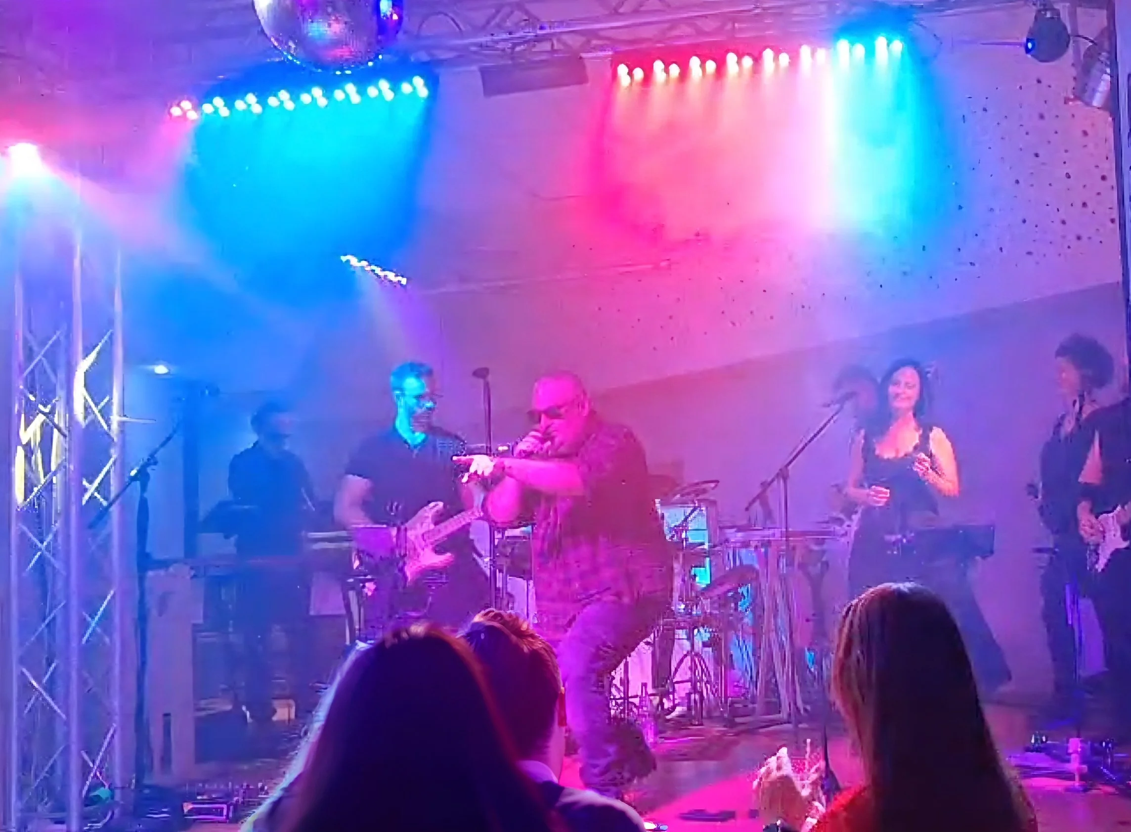 Menschen bei einem Konzert oder einer Party mit buntem Licht und Musik-Equipment im Hintergrund.