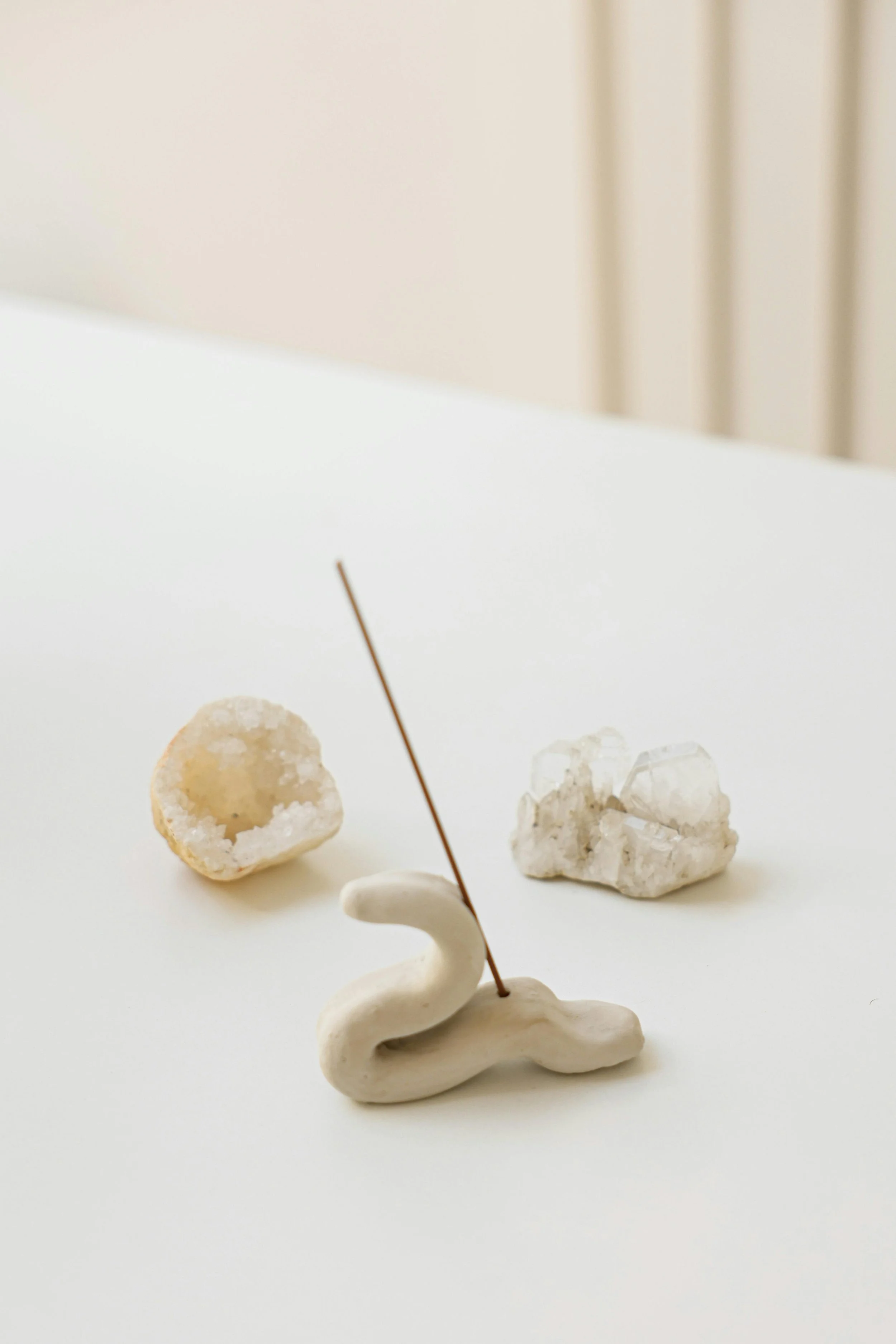 Decorative objects on a white surface, including a small swan figurine with a thin dark stick, a hollow rock, and a block of white crystal.