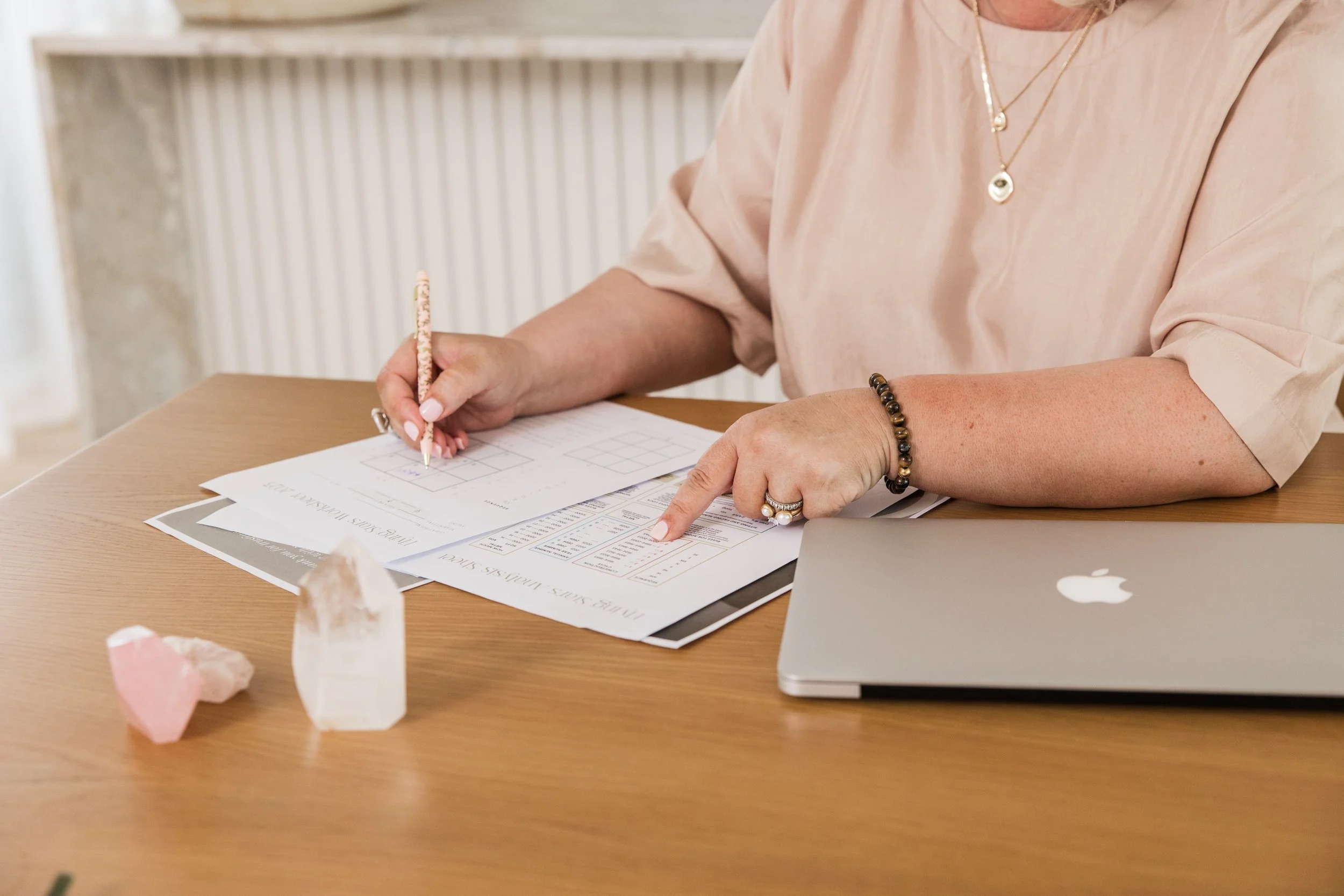 A person sitting at a desk writing on paperwork with a pen, with a laptop and decorative stones on the desk.
