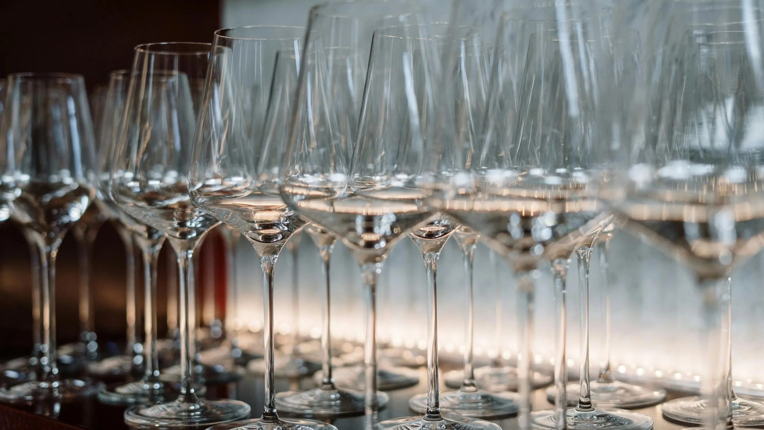 rows of clean wine glasses lined up on a bar counter with soft natural light and shallow depth of field