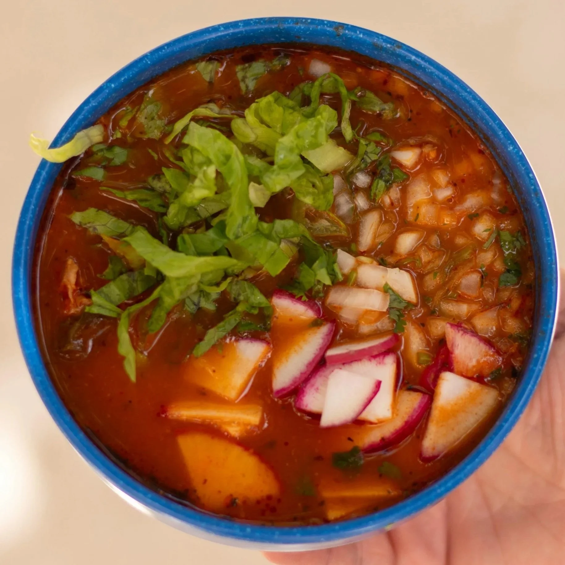 Bowl of red pozole with cilantro and radish garnish