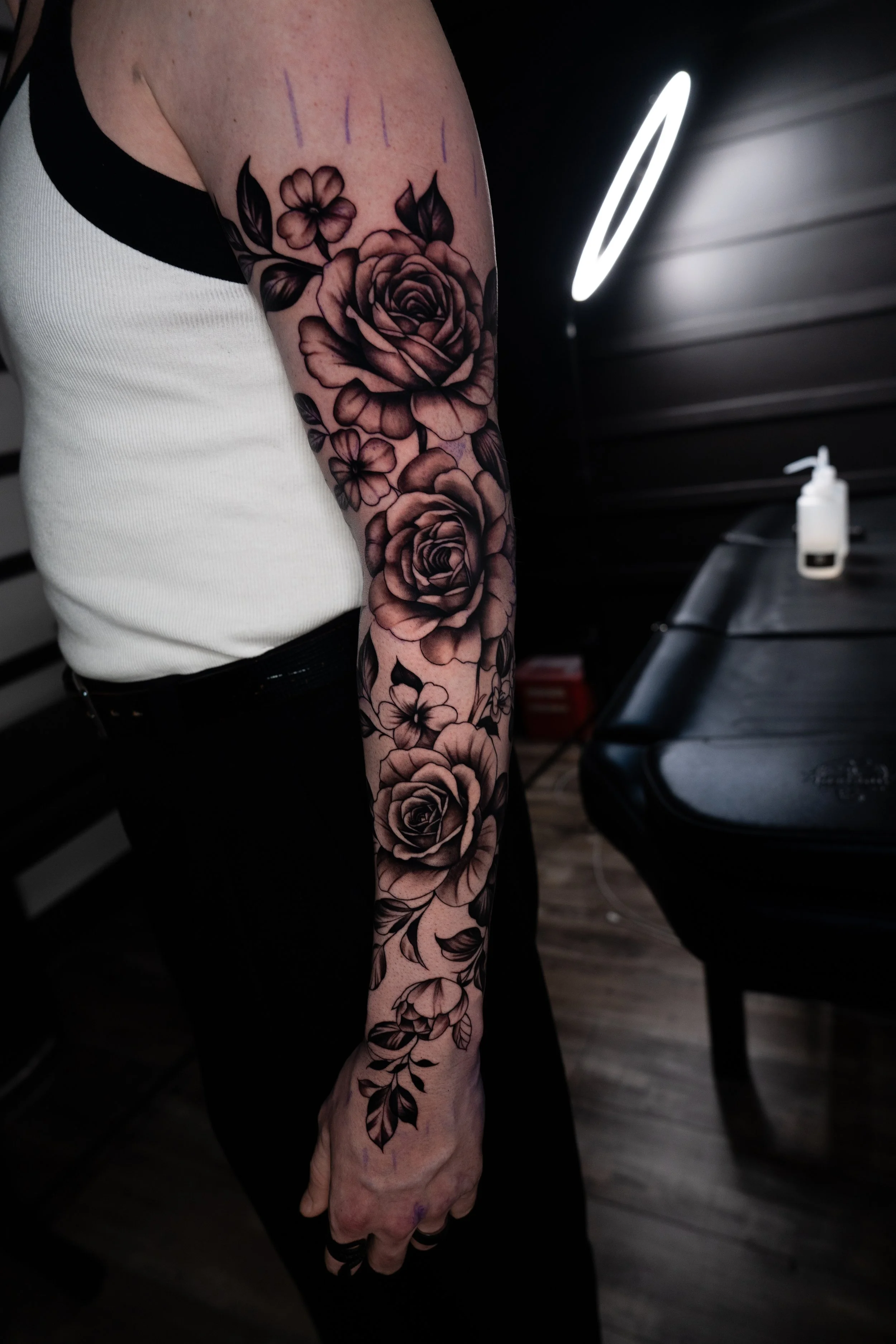 A person's arm with a black and gray floral tattoo featuring roses and leaves.