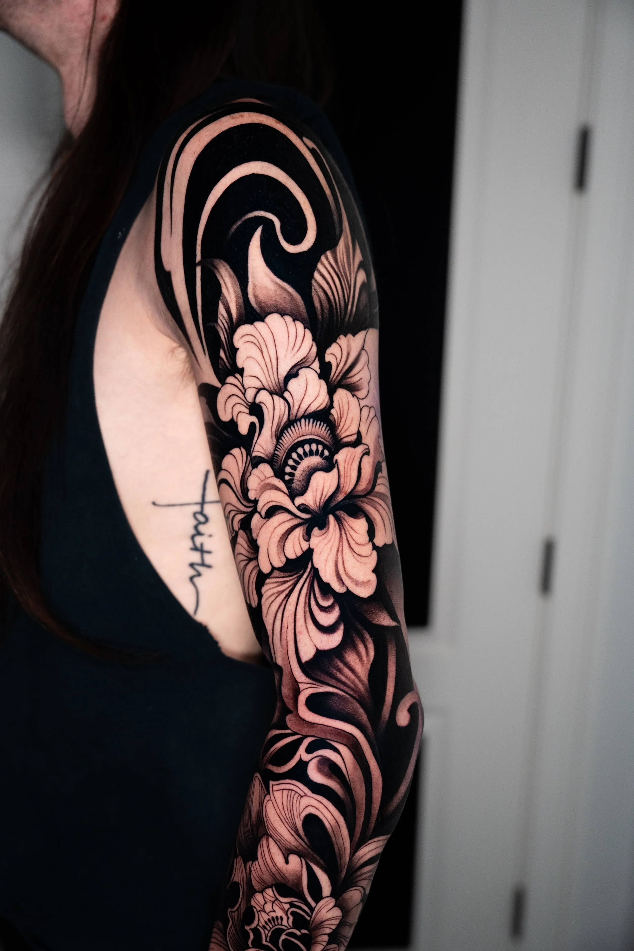 Close-up of a person's upper arm with a detailed black and pink floral sleeve tattoo.