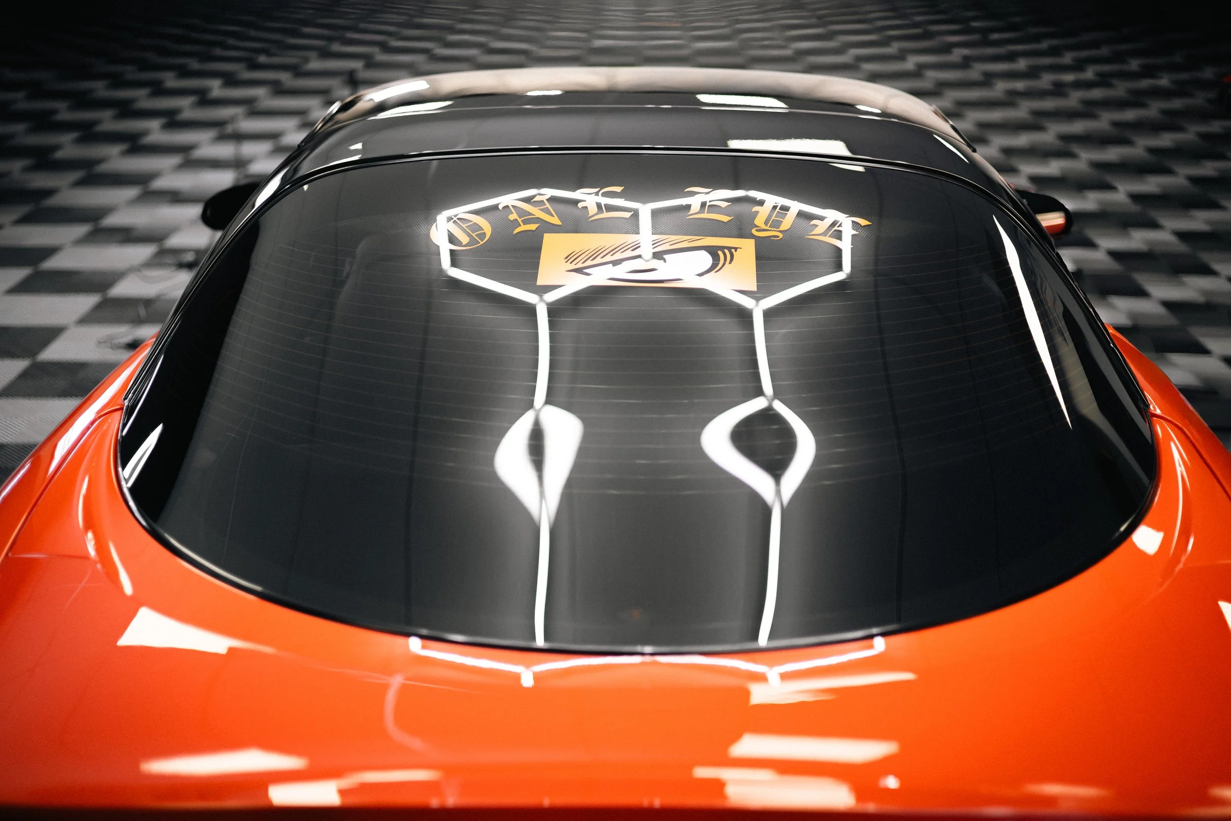 Top view of an orange sports car with a black rear window displaying a decal with the word 'AVE' and a stylized design.
