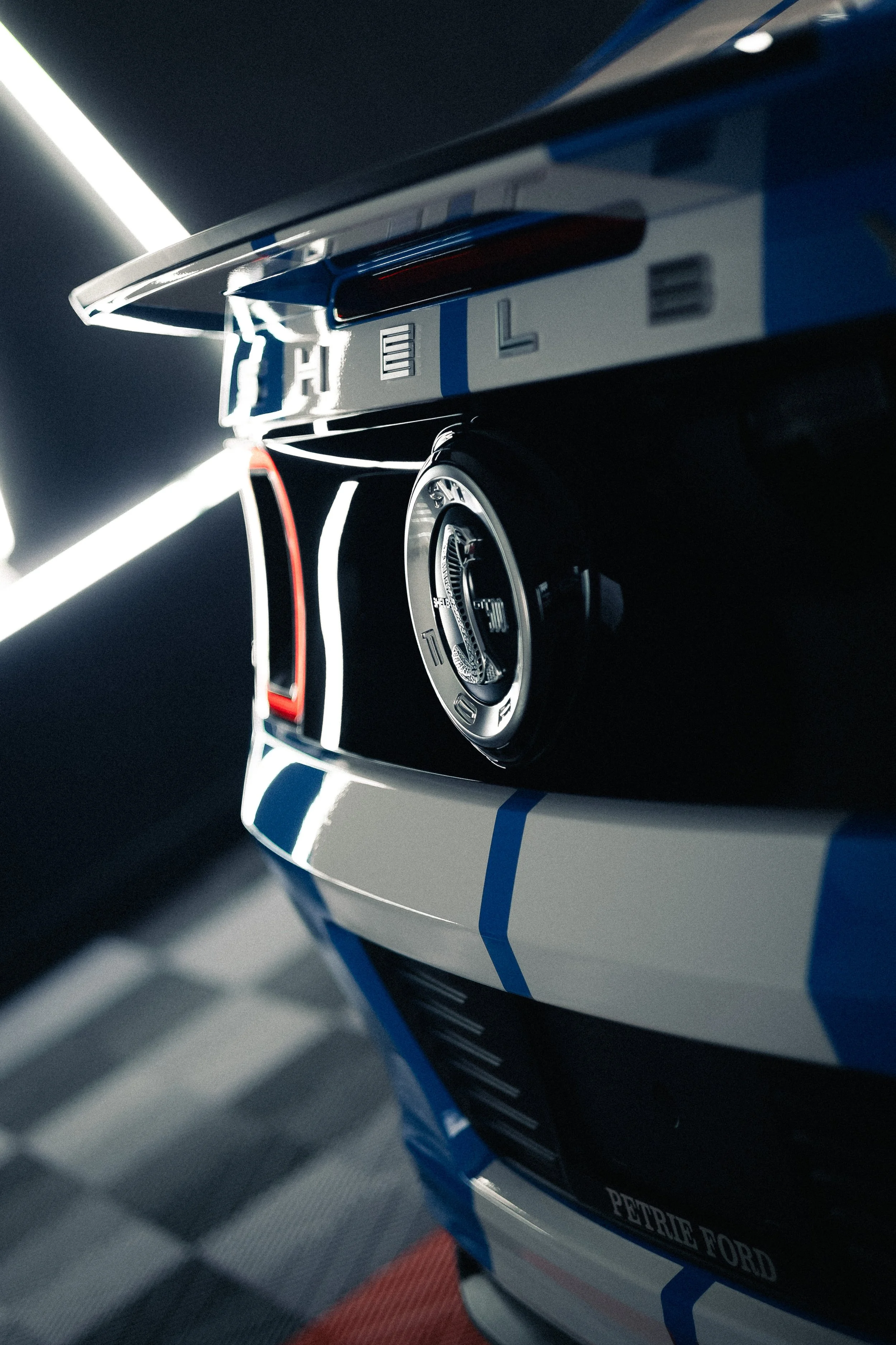 Close-up of race car with Petrite Ford branding, racing stripes, and a sleek design on a racetrack with a blurred background.