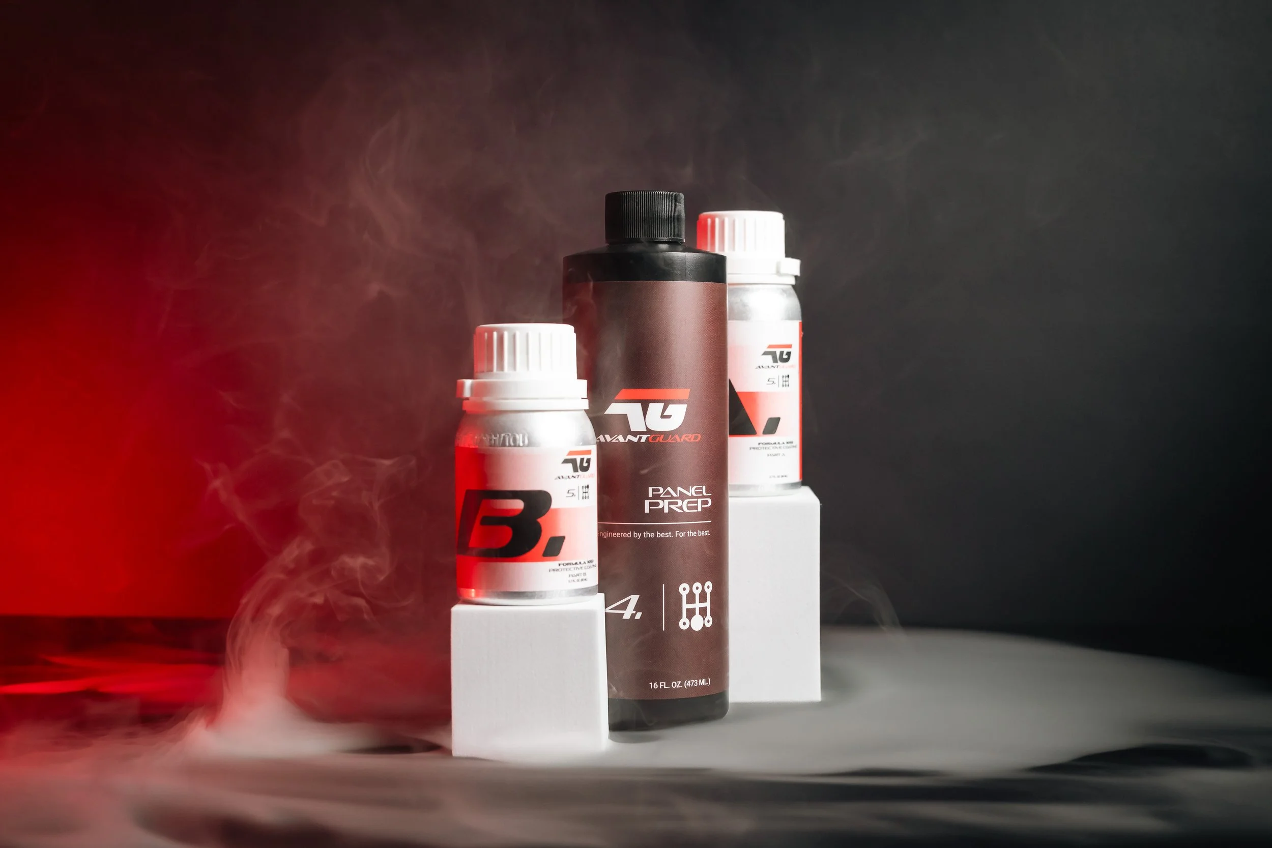 Three bottles of automotive Fluid Trainer products with dark background, red and white labels, and swirling smoke or vapor around them.