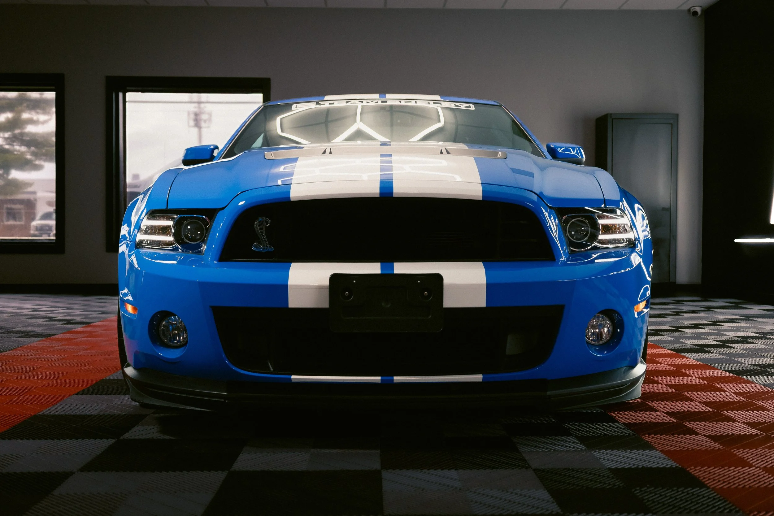 Blue sports car with white racing stripes displayed inside a showroom.