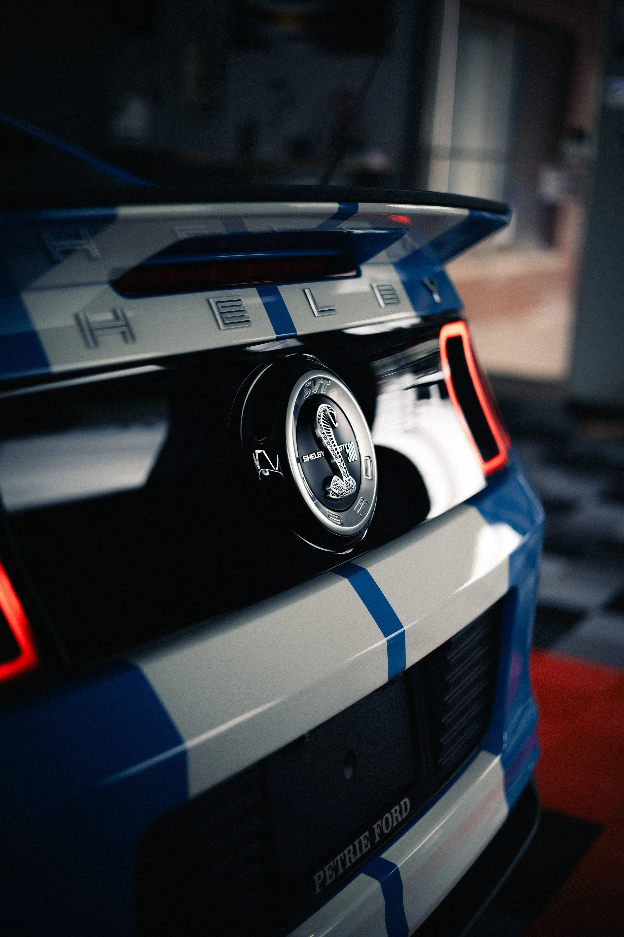 Close-up of a blue and white model race car with a Shelby Cobra emblem on the wheel and PETROLE FORD branding on the side.