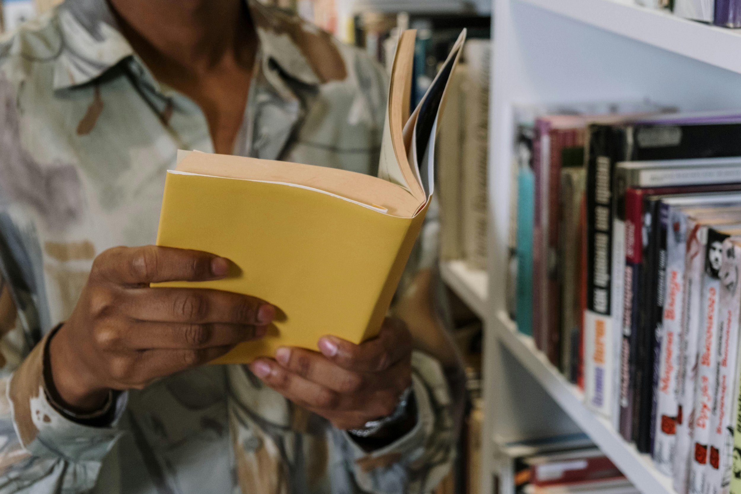 Person holding a yellow book while browsing bookshelves in a bookstore.