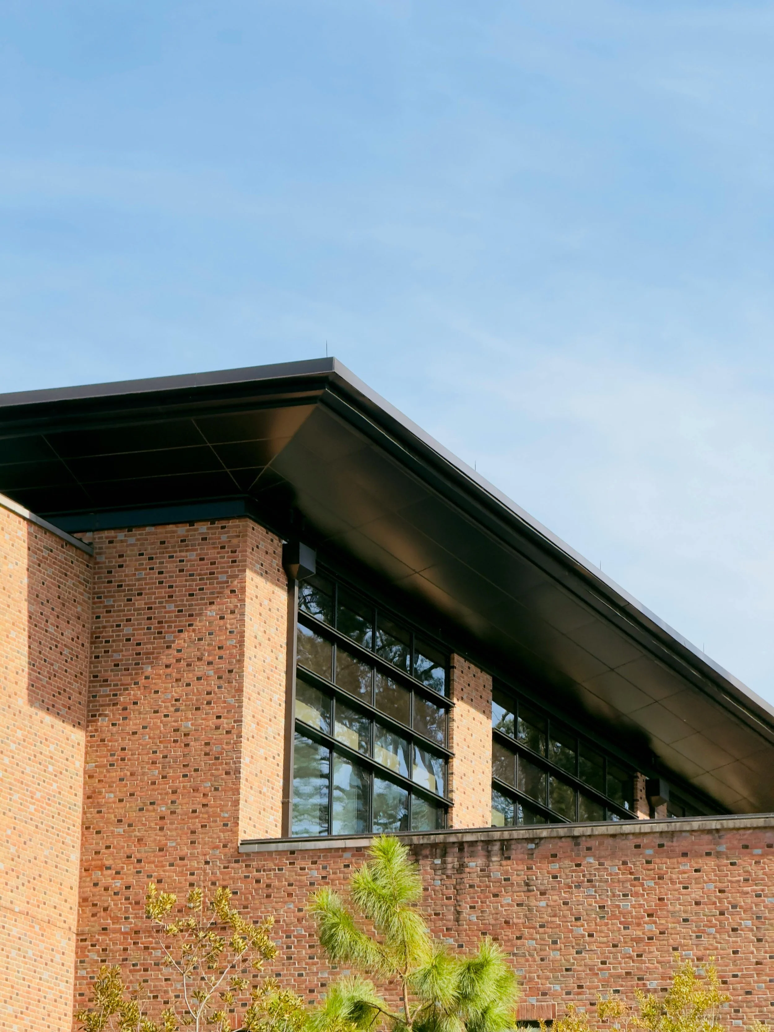 Close-up of a modern brick building with large glass windows and black overhang, under a blue sky.