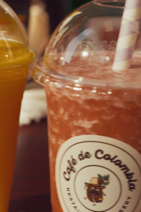 Jugos Naturales: Two colorful cold beverages with straws on a table, one orange and one pink, at Cafe de Colombia.