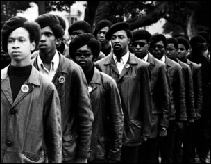 Historical black-and-white photograph of Black Panther Party members standing in a disciplined line, wearing their signature black berets and leather jackets, symbolizing organized resistance and the collective power of the movement.