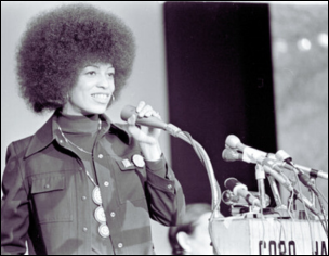 Angela Davis speaking into a microphone at a podium, showcasing a history of Black activism and public oratory.