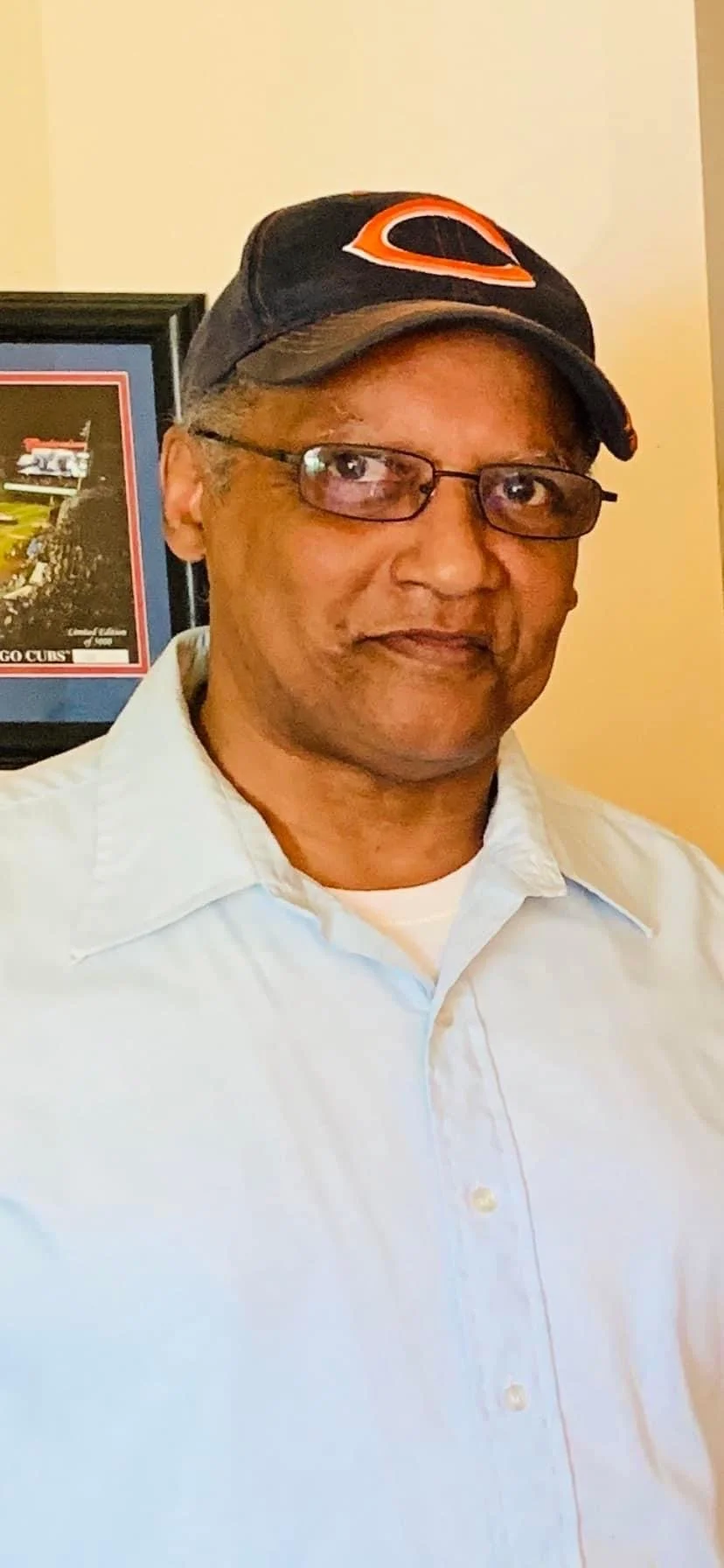 Photo of the author's father, Greg, smiling in a light blue button down and Chicago bears hat.