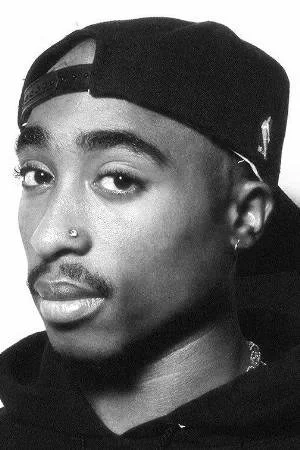 Close-up headshot of Tupac Shakur wearing a black backward baseball cap and a black hoodie. He has a nose stud and is looking slightly off-camera with a contemplative expression.