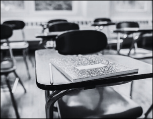 Black and white photo of a classroom desk with a composition notebook and pencil, symbolizing academic study.