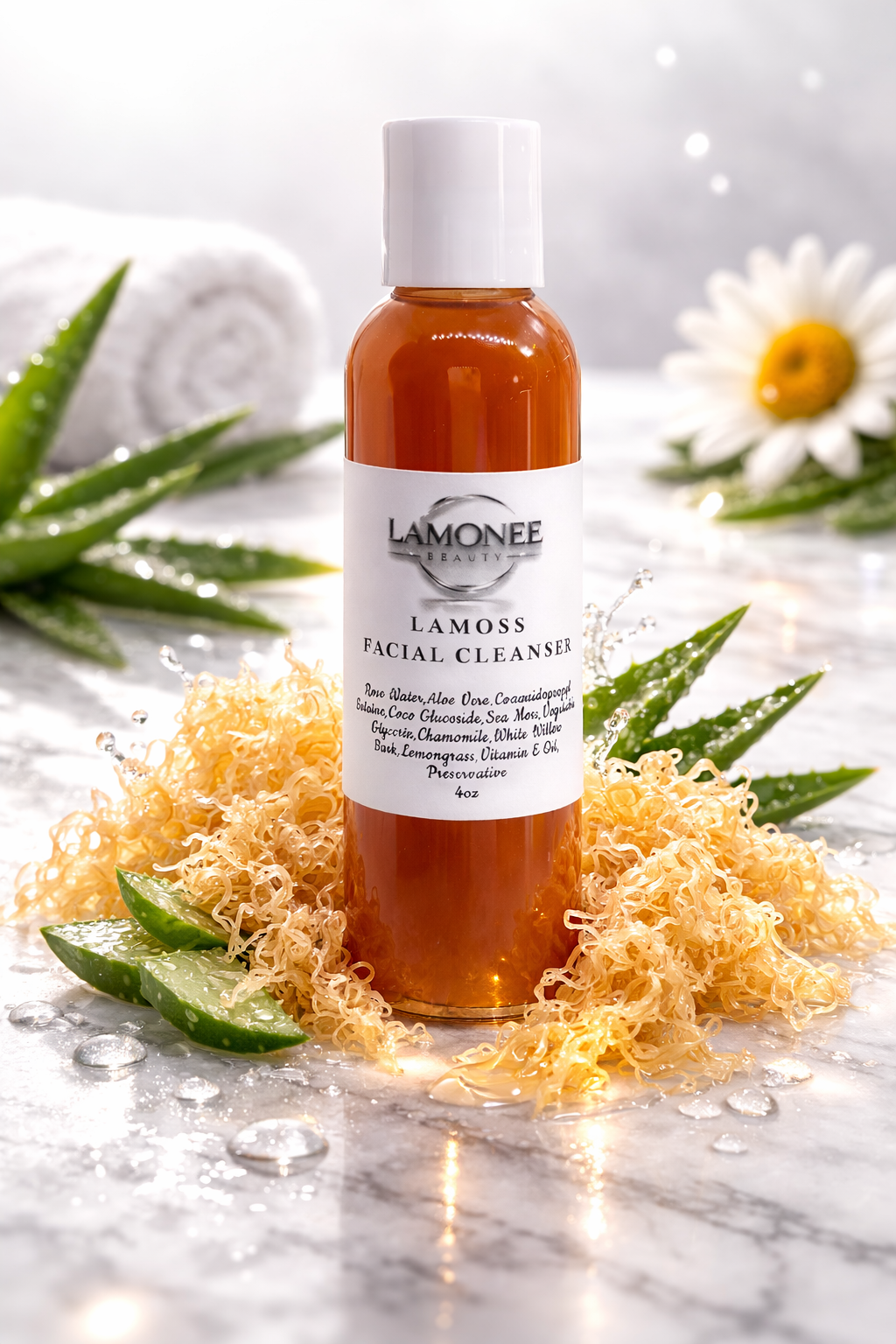 A bottle of Lamonee Beauty Lamoss facial cleanser surrounded by aloe vera, sea moss, and chamomile, with a white towel and daisy in the background on a marble surface.