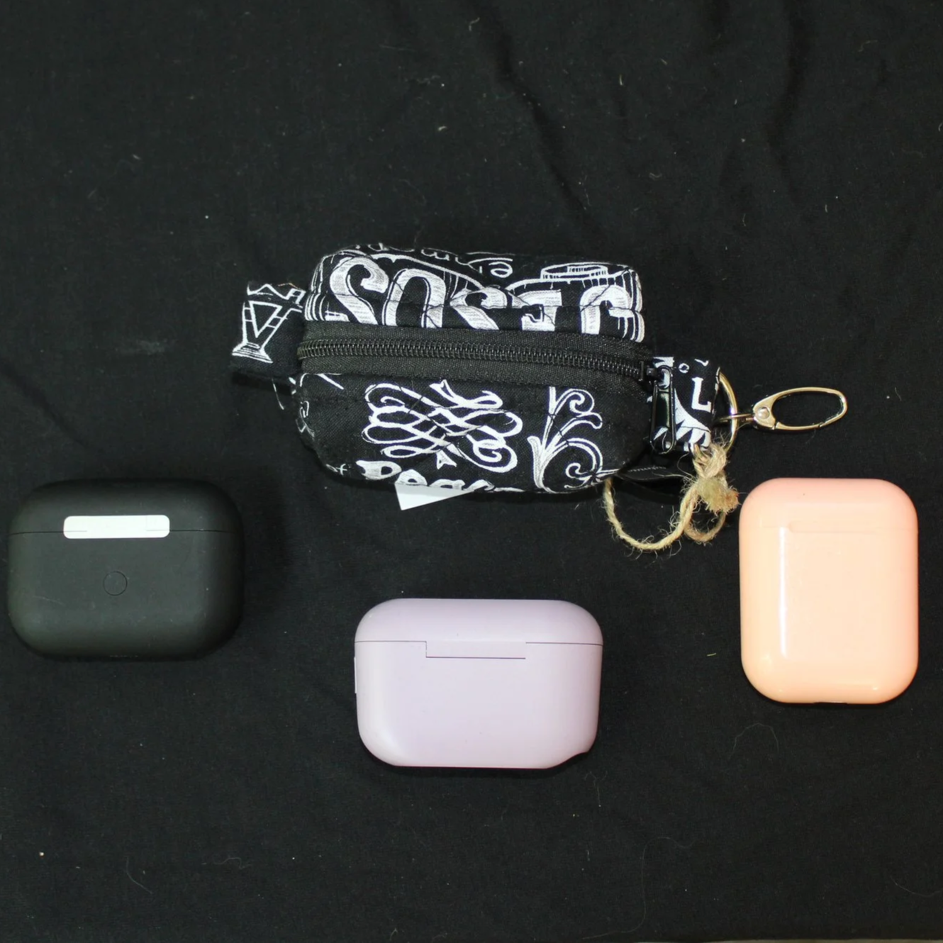 Top closed view of the King of Kings Bag Charm showing names of Jesus print fabric displayed with three different sized earbud cases for sizing reference.