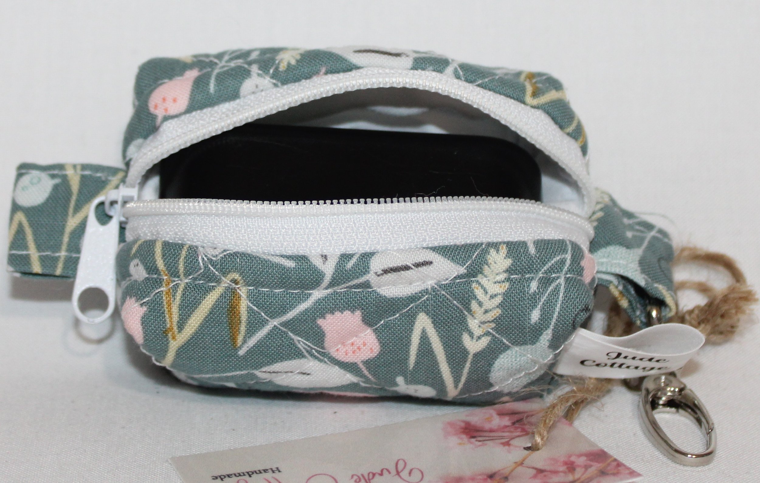 Open top view of the Meadow Breeze Bag Charm featuring a sage green background with spring floral print shown with a J Lab earbud case inserted for size reference.