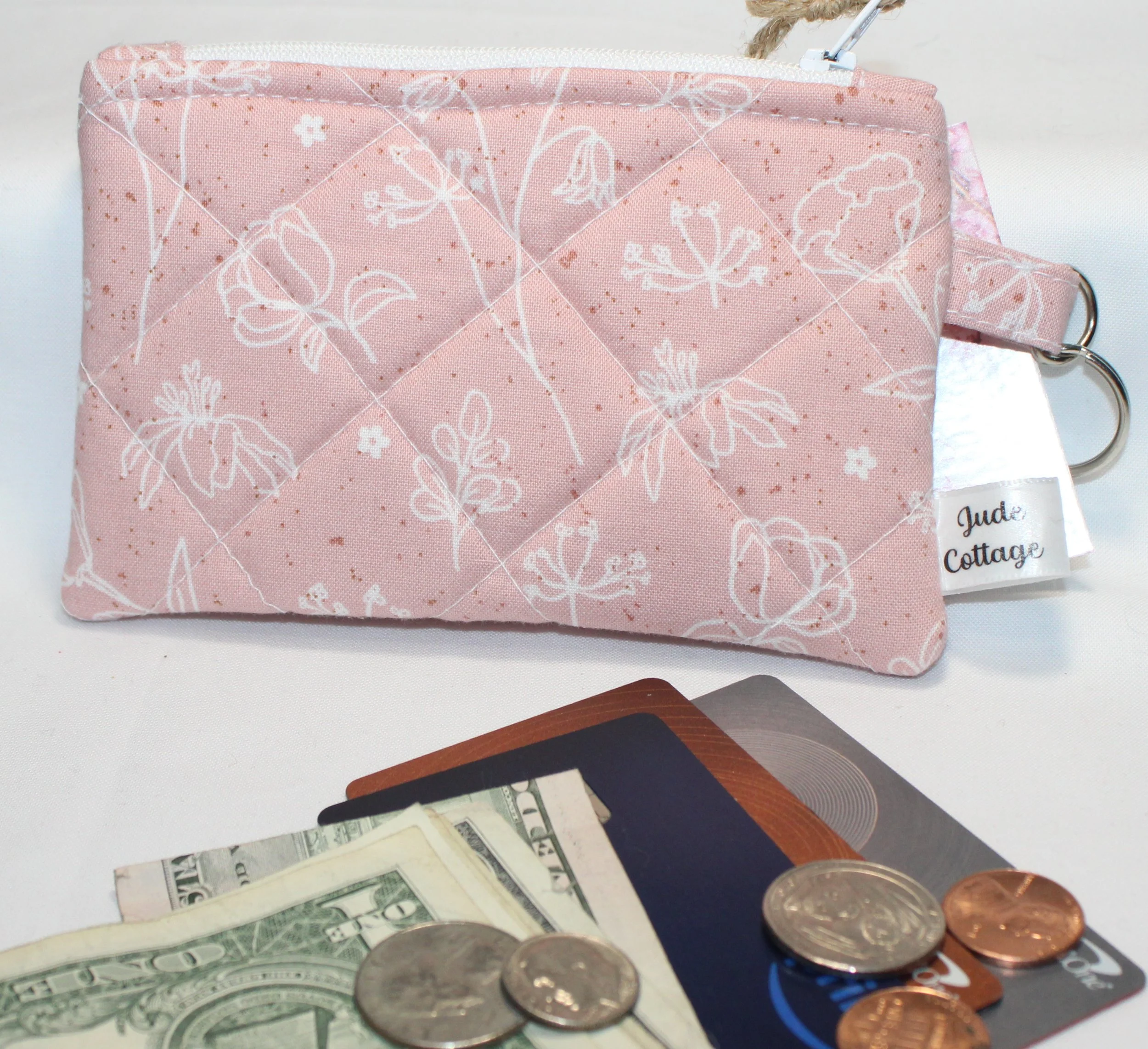 Small quilted keychain wallet with a pink background and white floral design, zipper closure, and metal key ring.