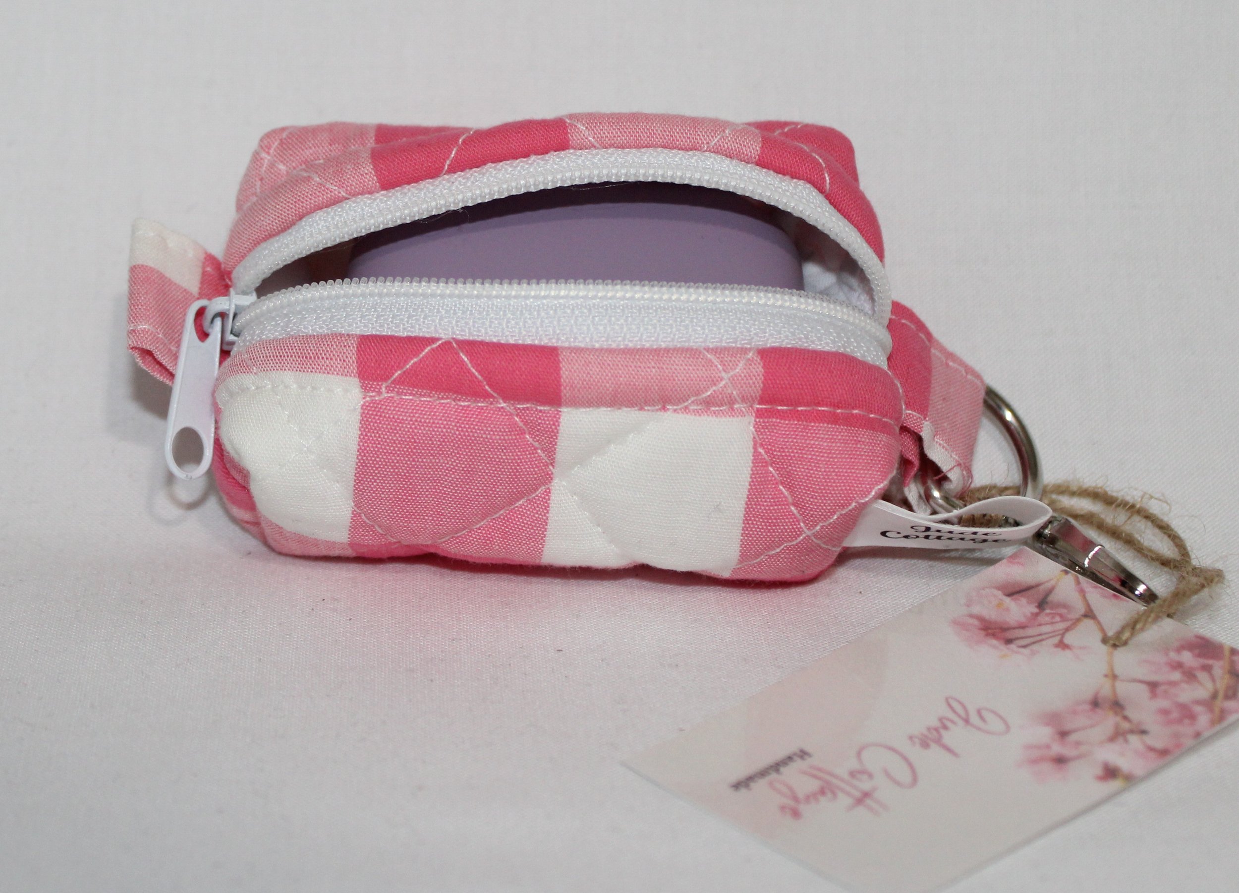 Top open view of the Sophie Bag Charm featuring a pink and white check fabric shown with a J Lab earbud case inserted to demonstrate sizing.