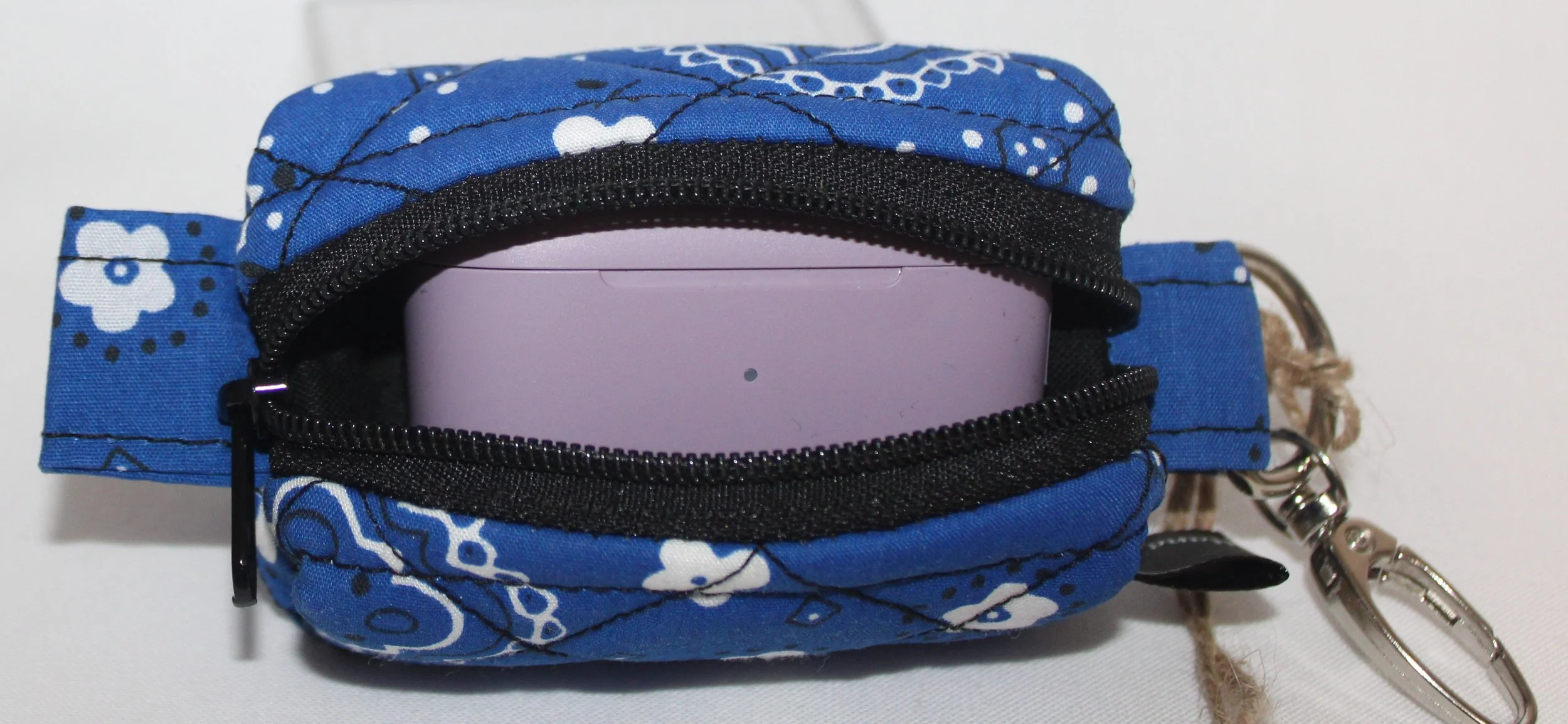 Top open view of the Blue Bandana Bag Charm showing its blue bandana‑print fabric with the zipper fully open. A pair of J Lap earbuds is placed inside the pouch for size and fit demonstration.