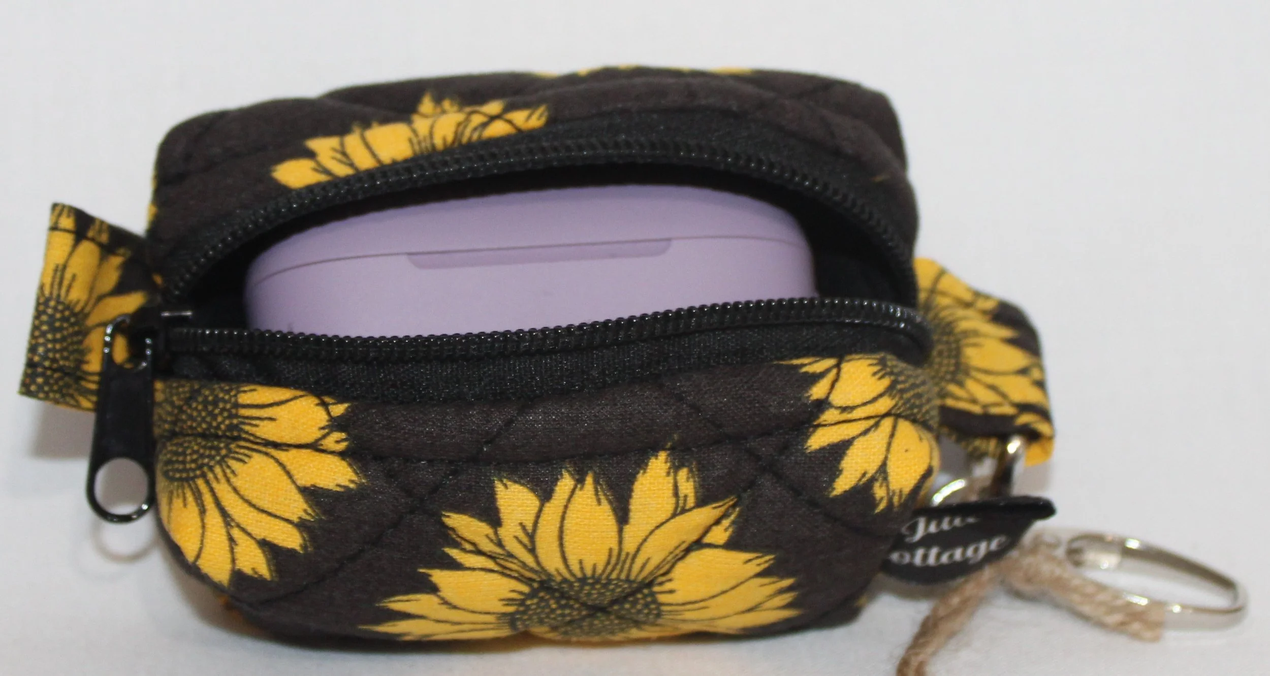 Top open view of the Midnight Sunflower Bag Charm featuring a black background fabric with bright golden yellow sunflowers, shown with a J Lab earbud case inserted to demonstrate fit.