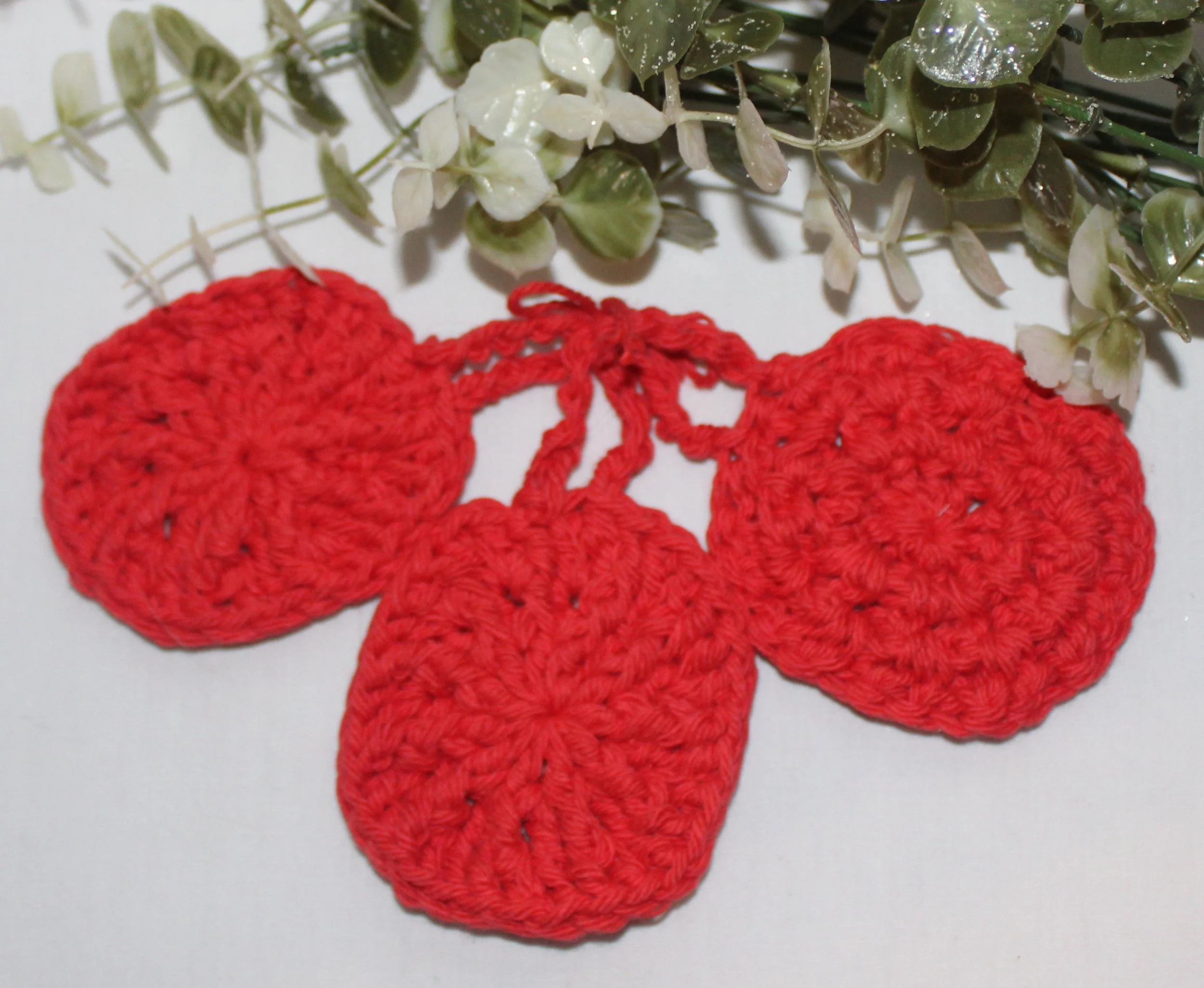 Close‑up of set of three round crocheted red facial scrubbies with a textured stitch pattern.