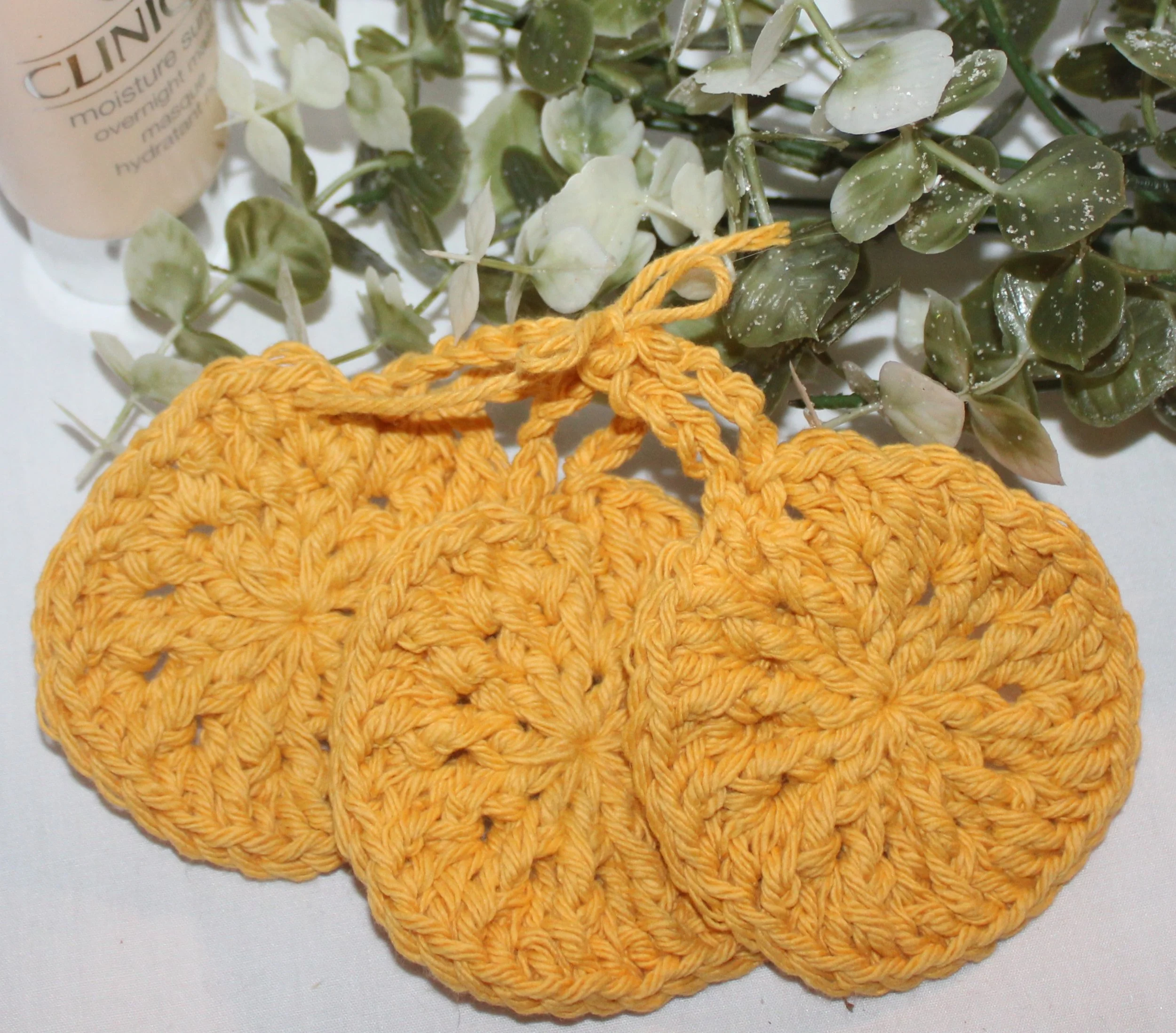 Close‑up of set of three round crocheted dandelion facial scrubbies with a textured stitch pattern.