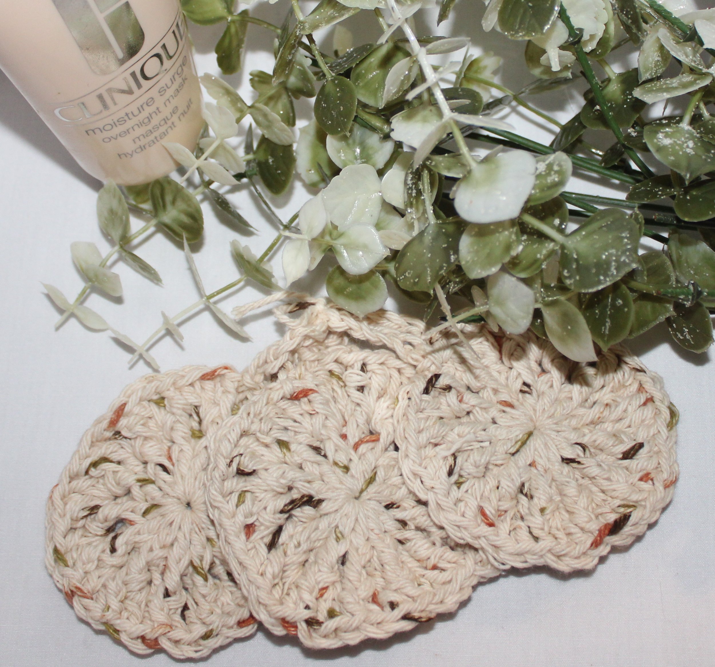Close‑up of set of three round crocheted beige facial scrubbies with a textured stitch pattern.