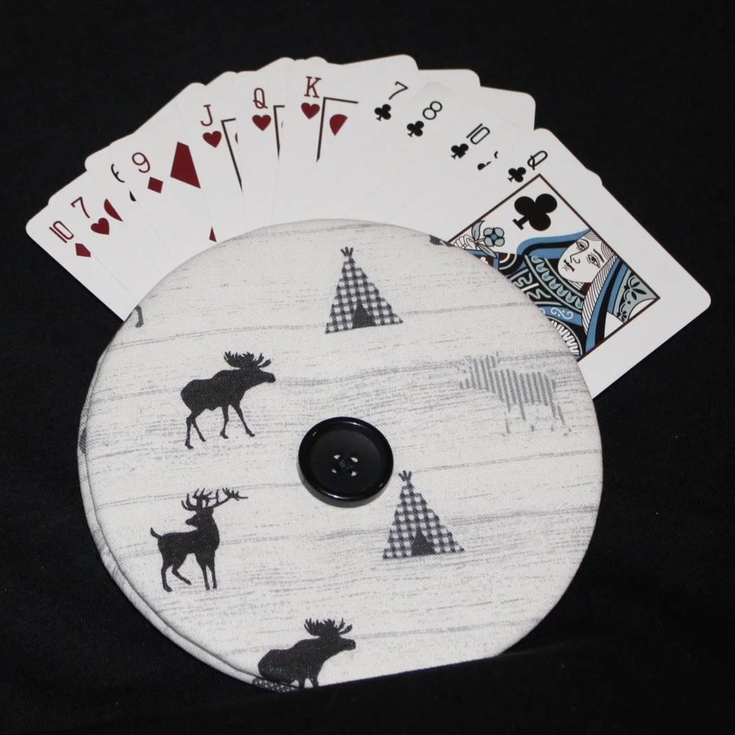 Front view of the Moose Camp Card Holder featuring moose, deer, and teepee motifs on white fabric shown in use with an array of playing cards.