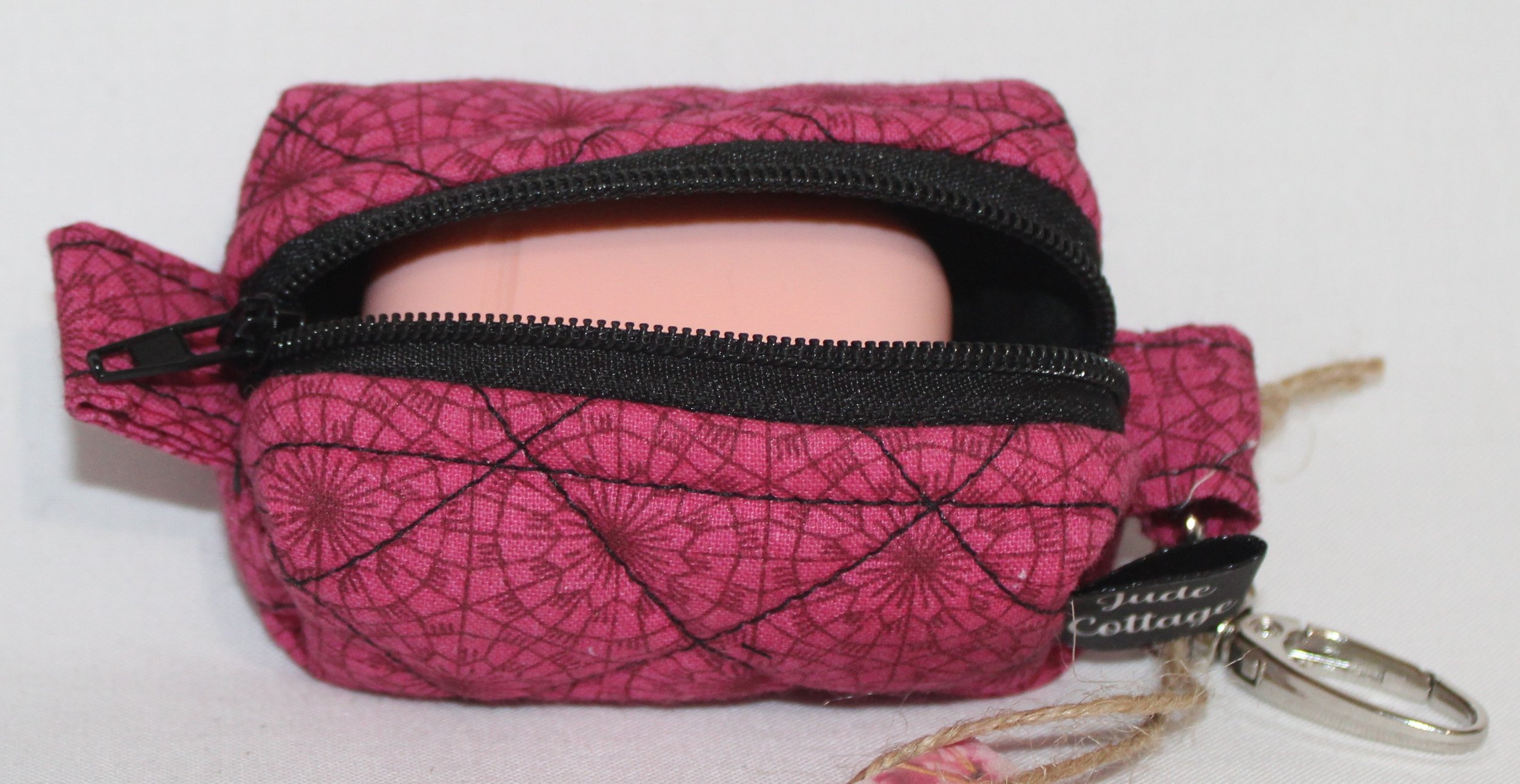 Front view of the Claire Bag Charm featuring a dark pink fabric with geometric print shown with an Airpod earbud case inserted to show sizing.