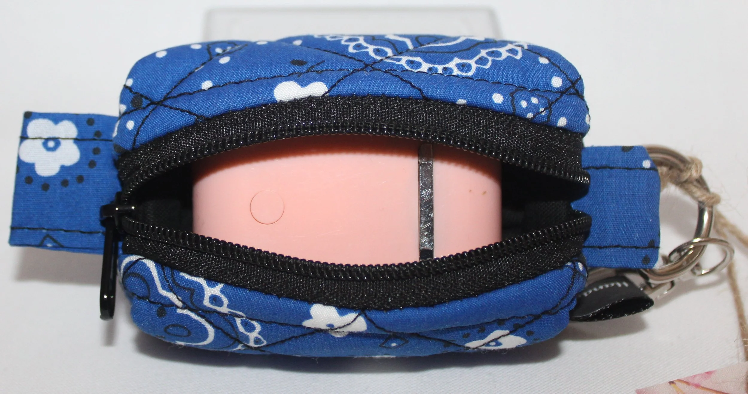 Top open view of the Blue Bandana Bag Charm showing its blue bandana‑print fabric with the zipper fully open. A pair of air pods earbuds are placed inside the pouch for size and fit demonstration.