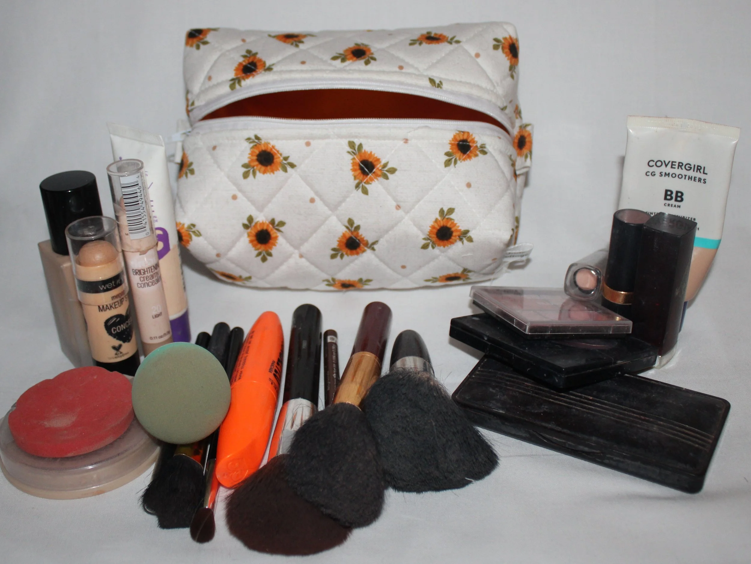 Top view of the open Sunflower Medley sunflower‑print quilted travel pouch with the gold interior showing and makeup items placed around it for scale.