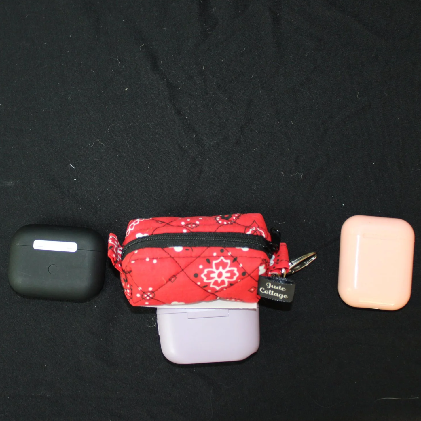Closed top view of the Red Bandana Bag Charm showing bandana print fabric shown with three different sized earbuds for size reference.