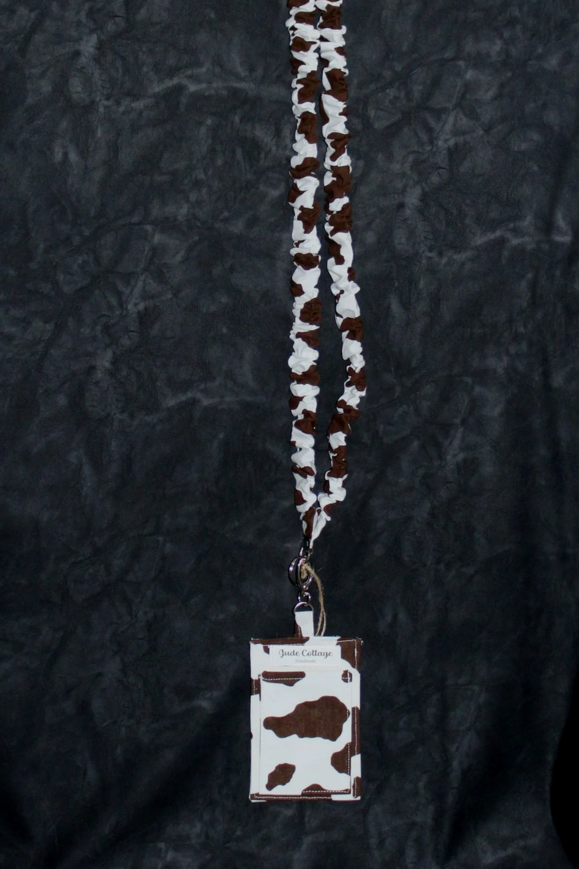 Full hanging view of the Brown Cow Scrunch Lanyard with Badge Holder featuring a white background with brown cow spots.