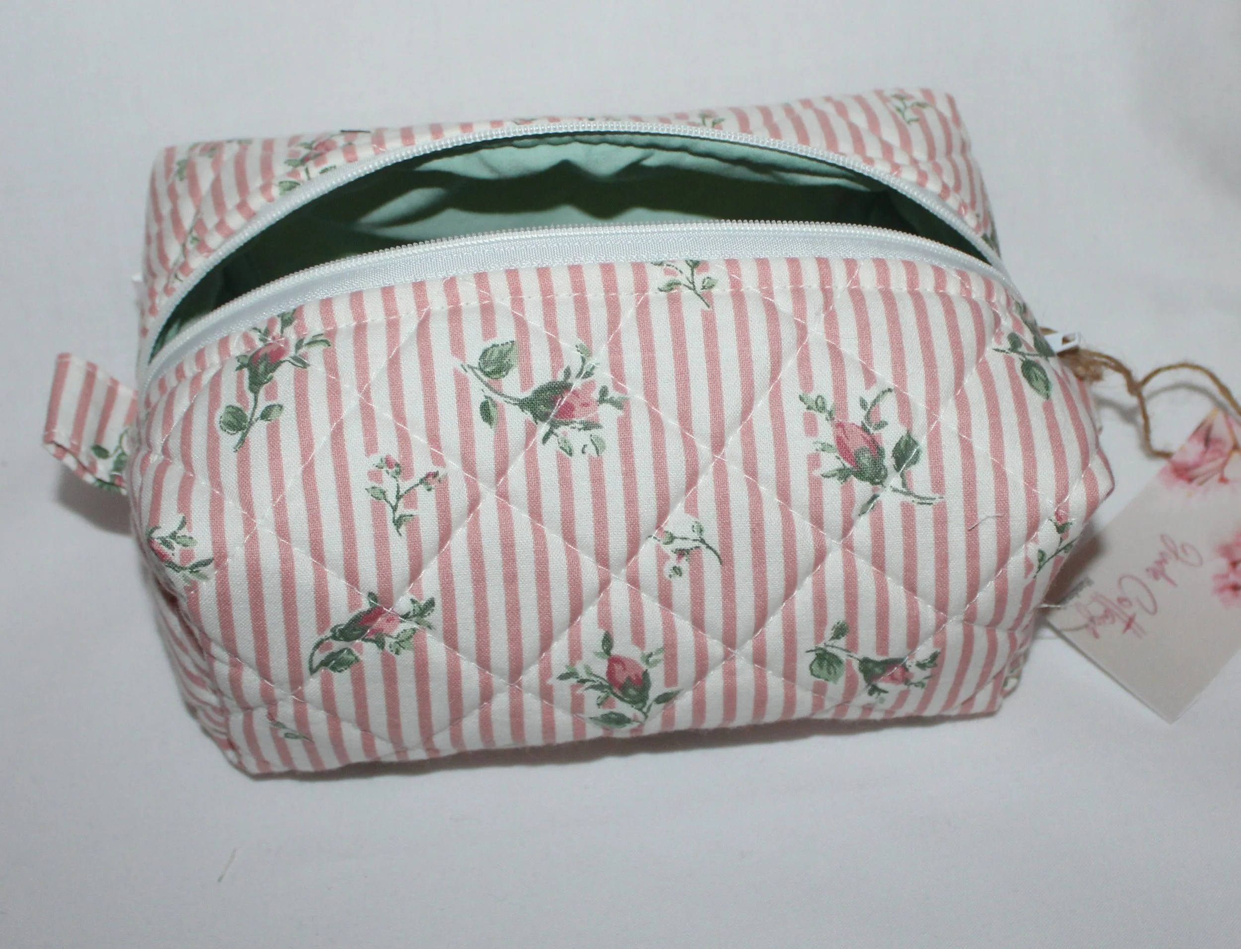 Front‑facing view of the Victoria quilted travel pouch in pink floral stripe fabric showing the open white zipper and mint green lining.
