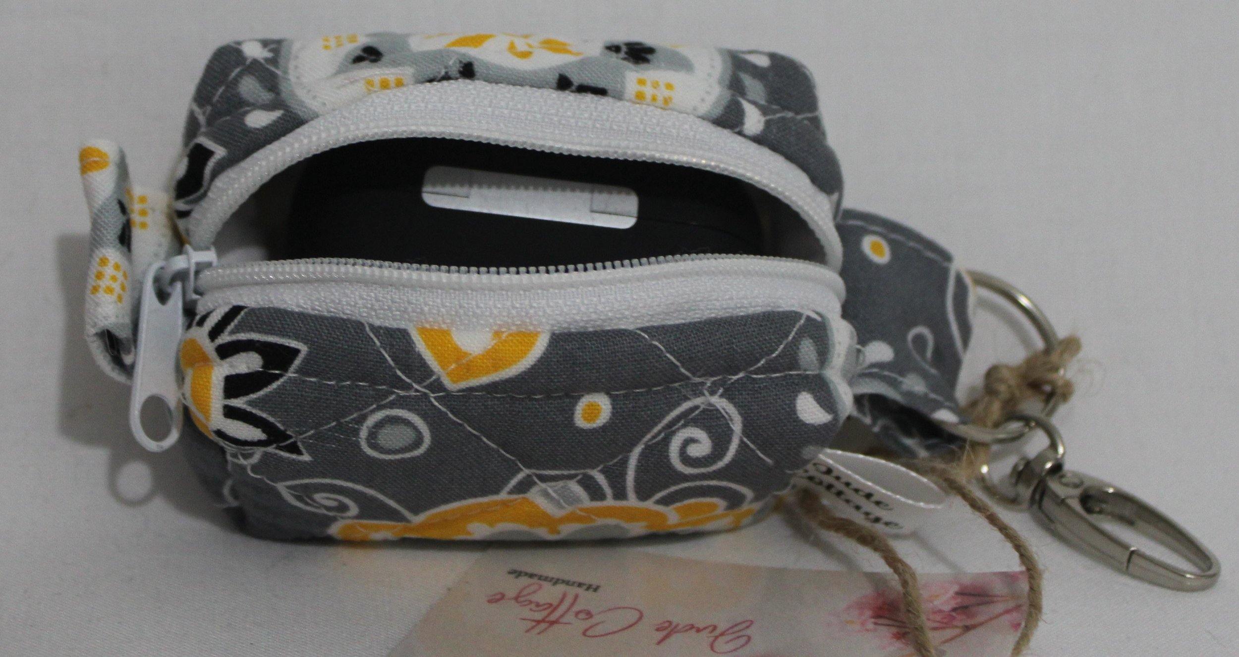 Top open view of the Medallion Bag charm featuring gray fabric with black, white and yellow floral print shown with an Airpod Pro case inserted for sizing reference.