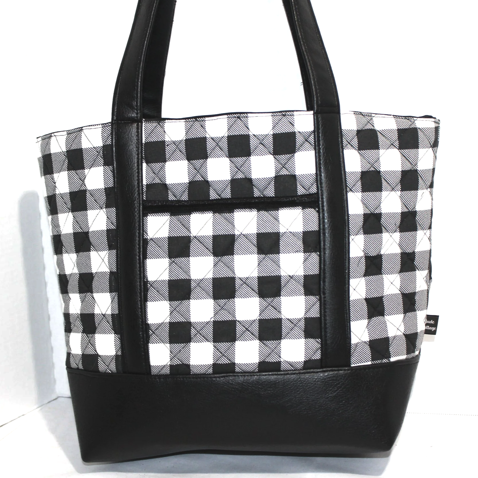 Front view of the Buffalo Black quilted tote showing the front slip pocket and faux leather straps and bottom, featuring a black and white buffalo plaid print.