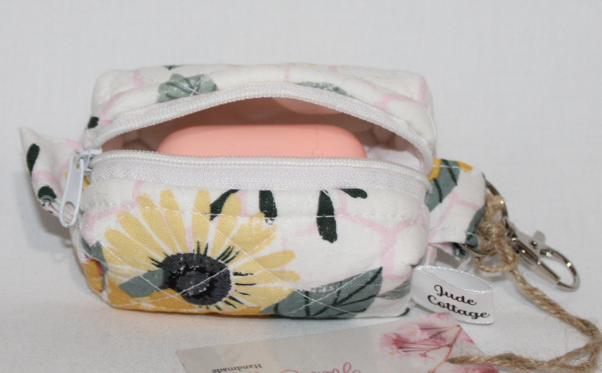 Open top view of the Honeycomb Sunflower Bag Charm featuring a white fabric with pink honeycombs and yellow sunflower print, shown with an Airpod earbud case inserted for sizing reference.