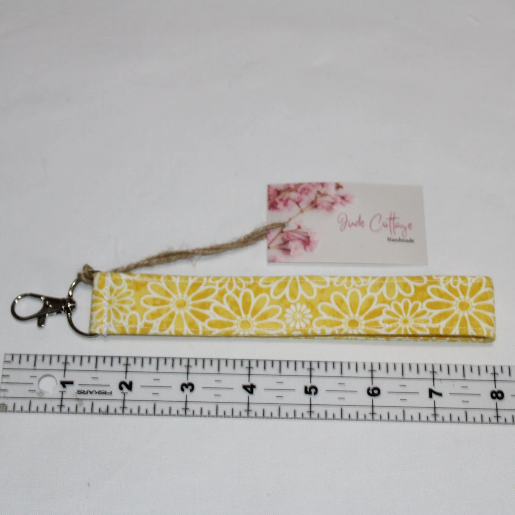 Gold Daisy Wristlet made from yellow fabric with a white daisy pattern, shown with an 8‑inch strap, metal clasp, shown with a ruler for size.