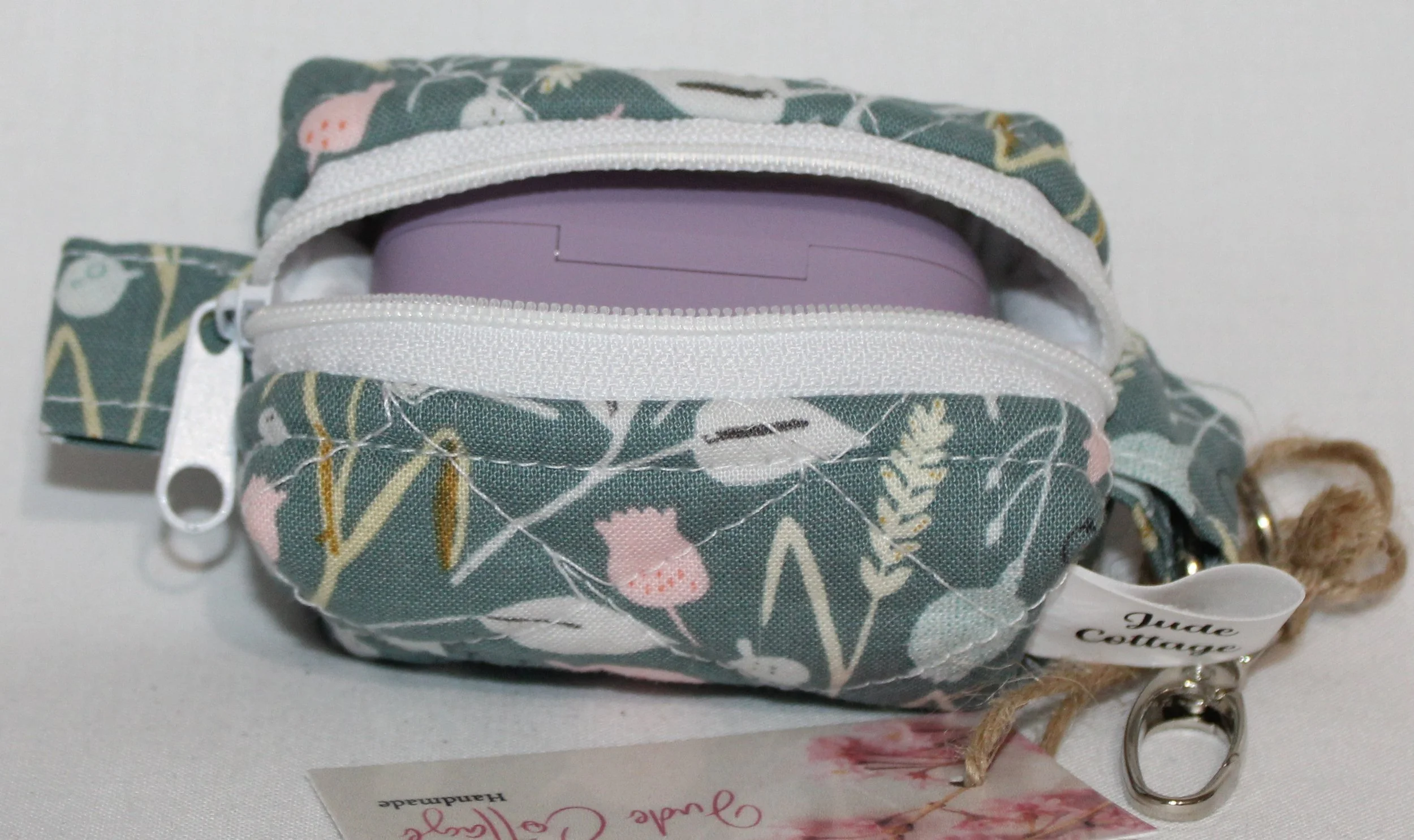 Open top view of the Meadow Breeze Bag Charm featuring a sage green background with spring floral print shown with a J Lab earbud case inserted for size reference.