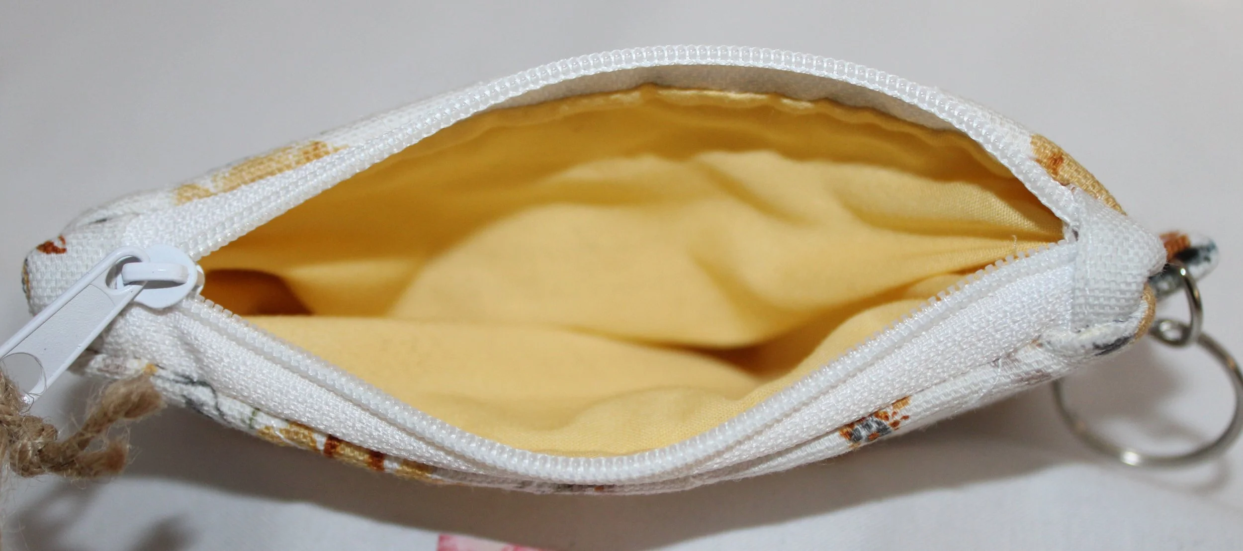 Top view of a quilted fabric wallet with multicolor wildflowers and a top zipper closure, showing yellow interior lining.