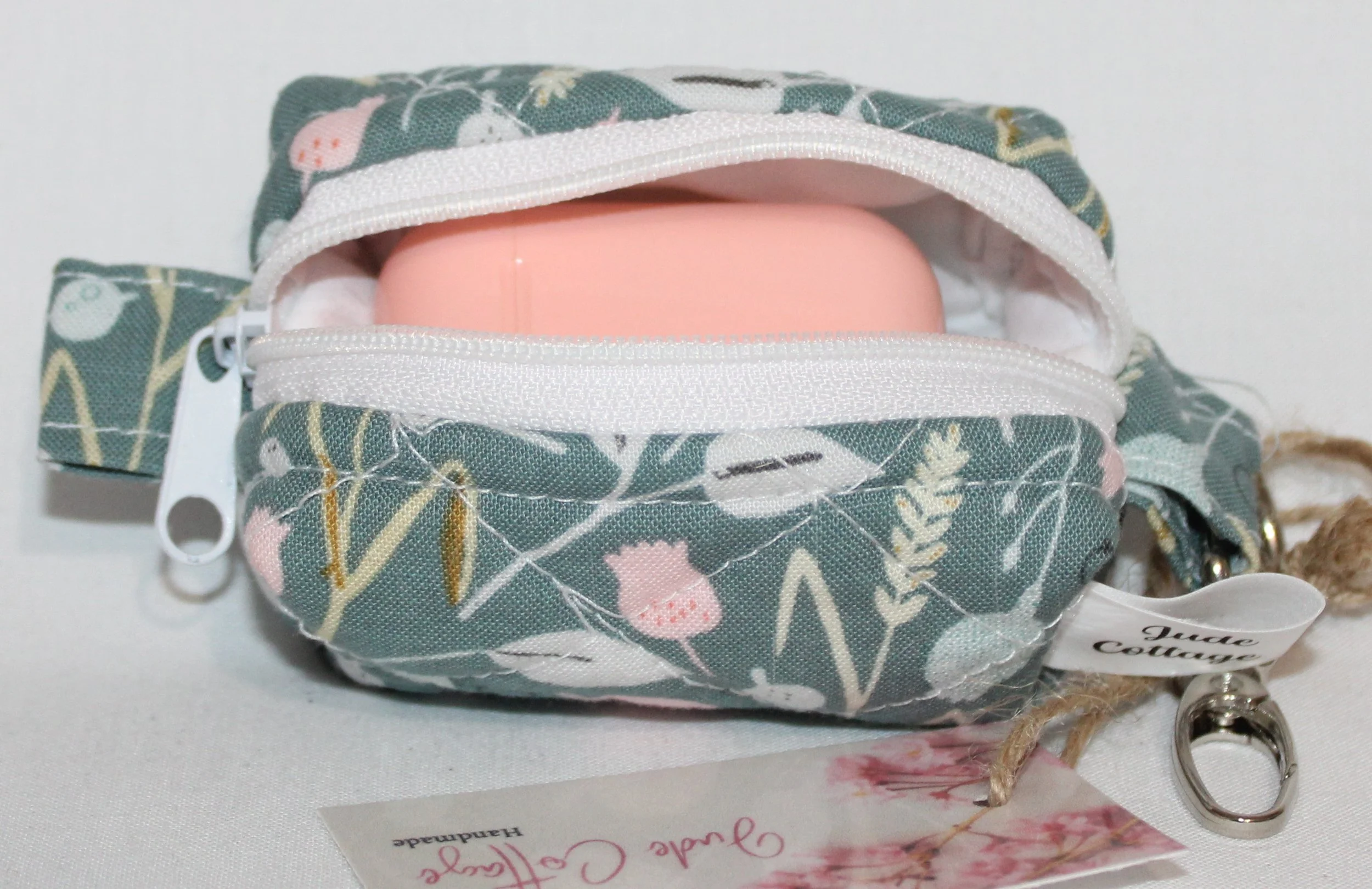 Open top view of the Meadow Breeze Bag Charm featuring a sage green background with spring floral print shown with an Airpod earbud case inserted for size reference.