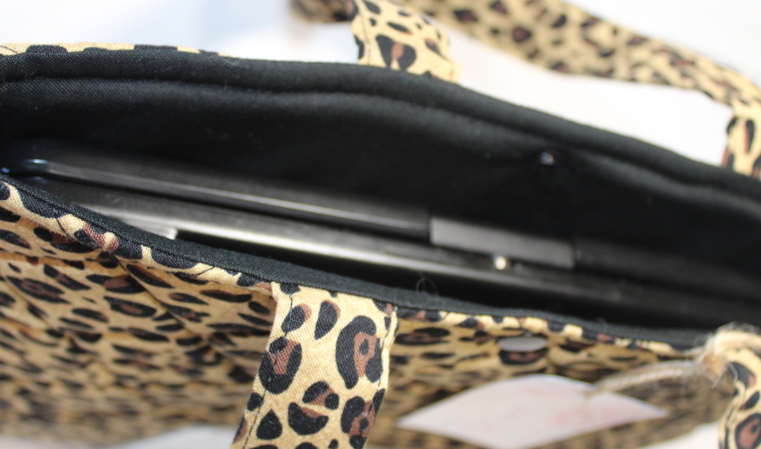 Top view of the Sahara quilted animal-print sleeve with cheetah print fabric, two carry handles, a snap closure, and a tablet inserted.