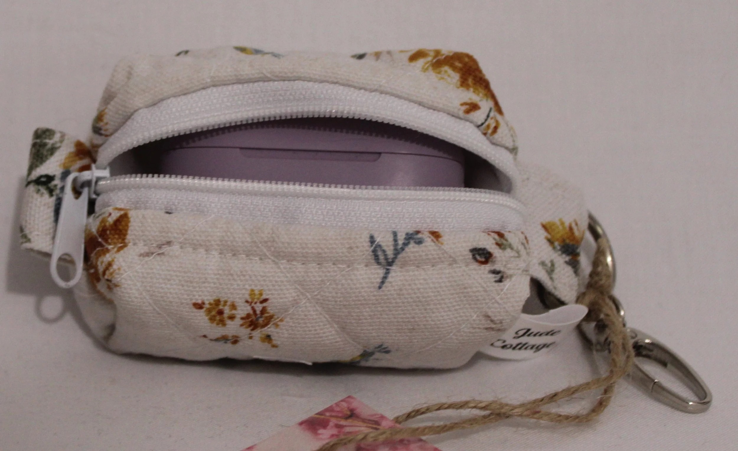 Top open view of the Dandelion Blue Bag Charm featuring assorted dandelions on an off white background and shown with a set of J Lab earbuds inserted for size reference.